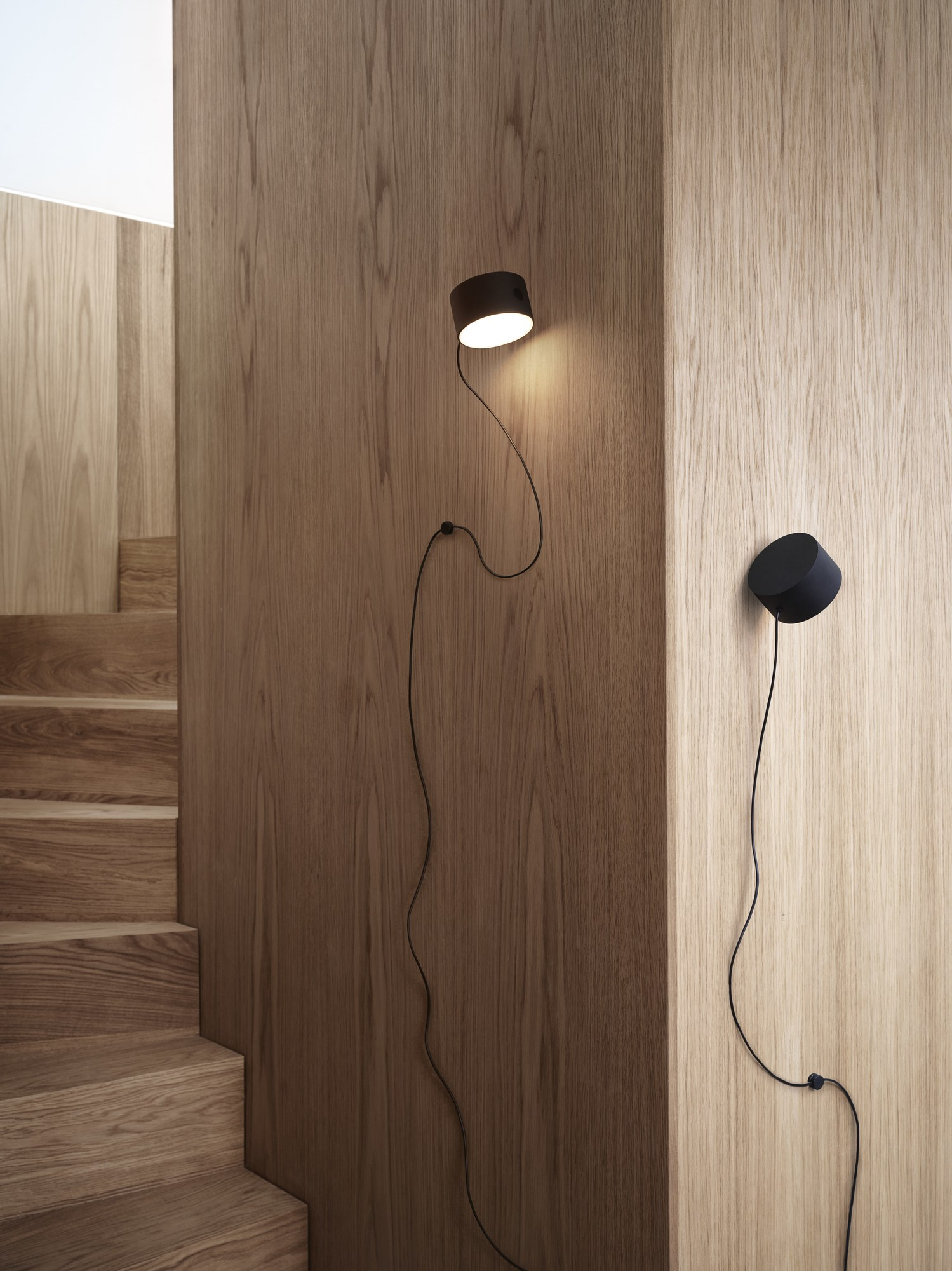 Nahaufnahme von zwei Muuto Post Wall Lamp Wandleuchten in Schwarz an einer Holzwand.