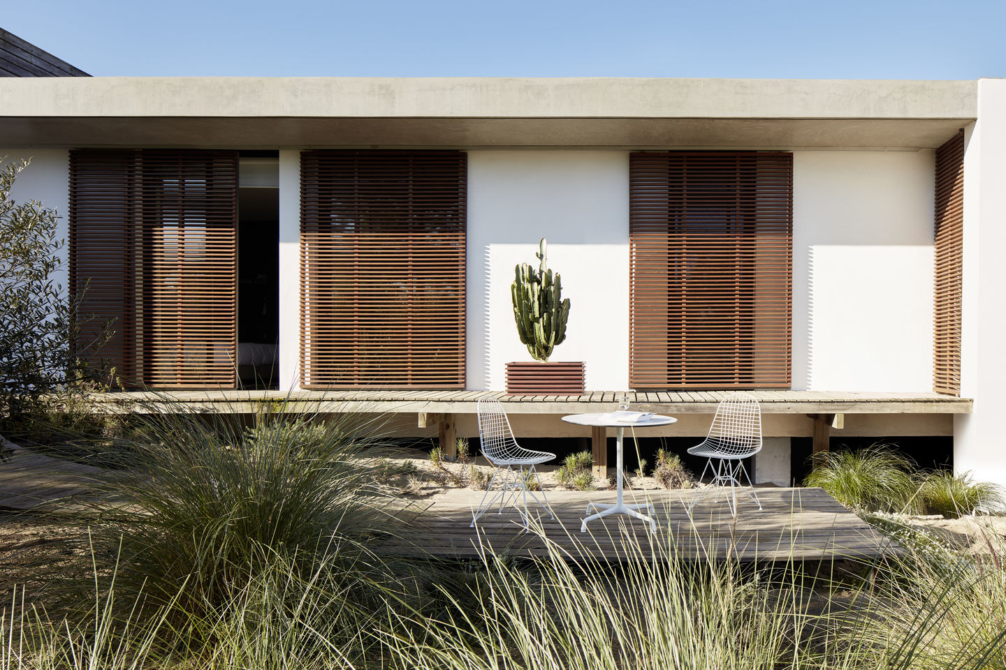 Zwei DKR Wire Chairs von Vitra mit Sitzpolster auf einer Holzterrasse vor modernem Haus.