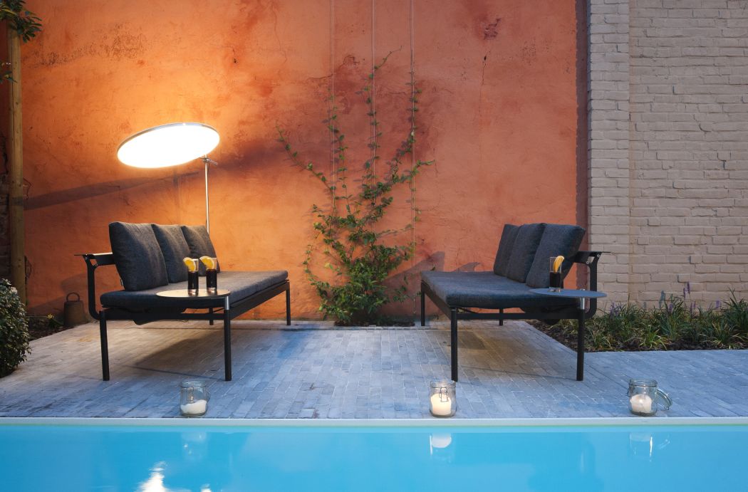 Sol + Luna Outdoor-Sonnenliege von Extremis neben Pool, mit Getränken und stimmungsvoller Beleuchtung.