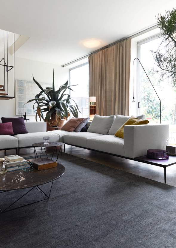 Helles Ecksofa mit Kissen in modernem Wohnzimmer mit Teppich und Beistelltischen.
