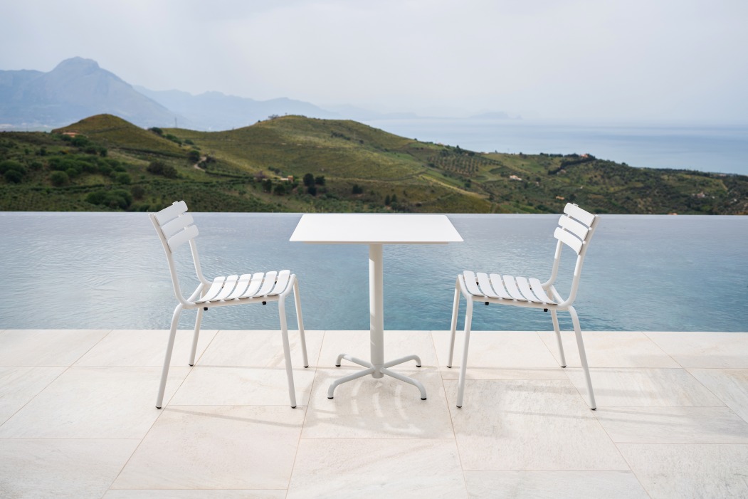 Zwei weiße Alua Dining Stühle von Houe und ein Tisch vor einem Infinity-Pool.