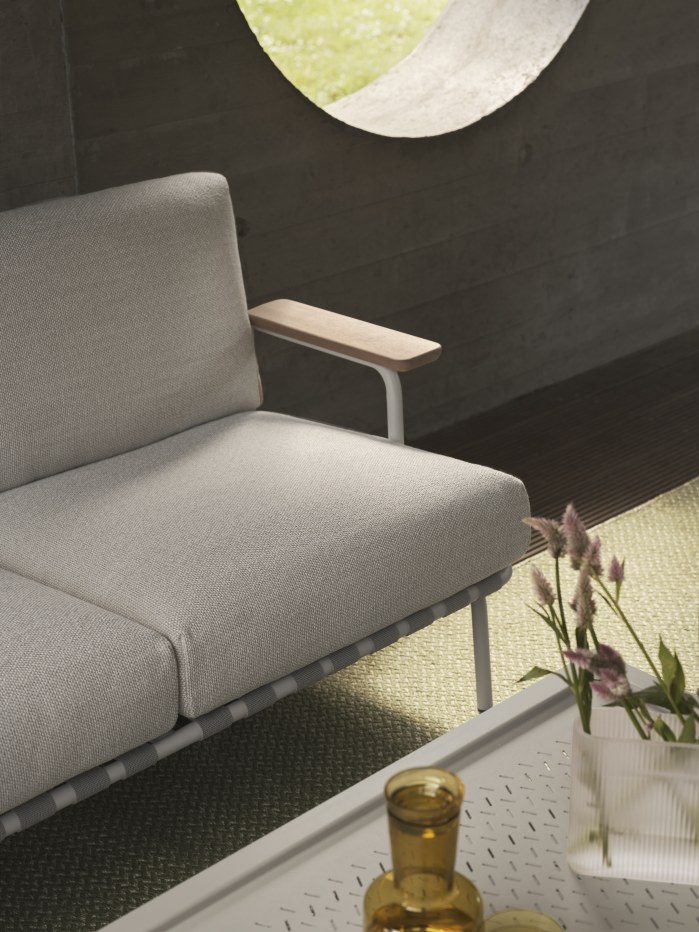 Detailaufnahme des Muuto Settle Outdoor Sofas (2-Sitzer) mit hellgrauem Bezug und Holzarmllehne.