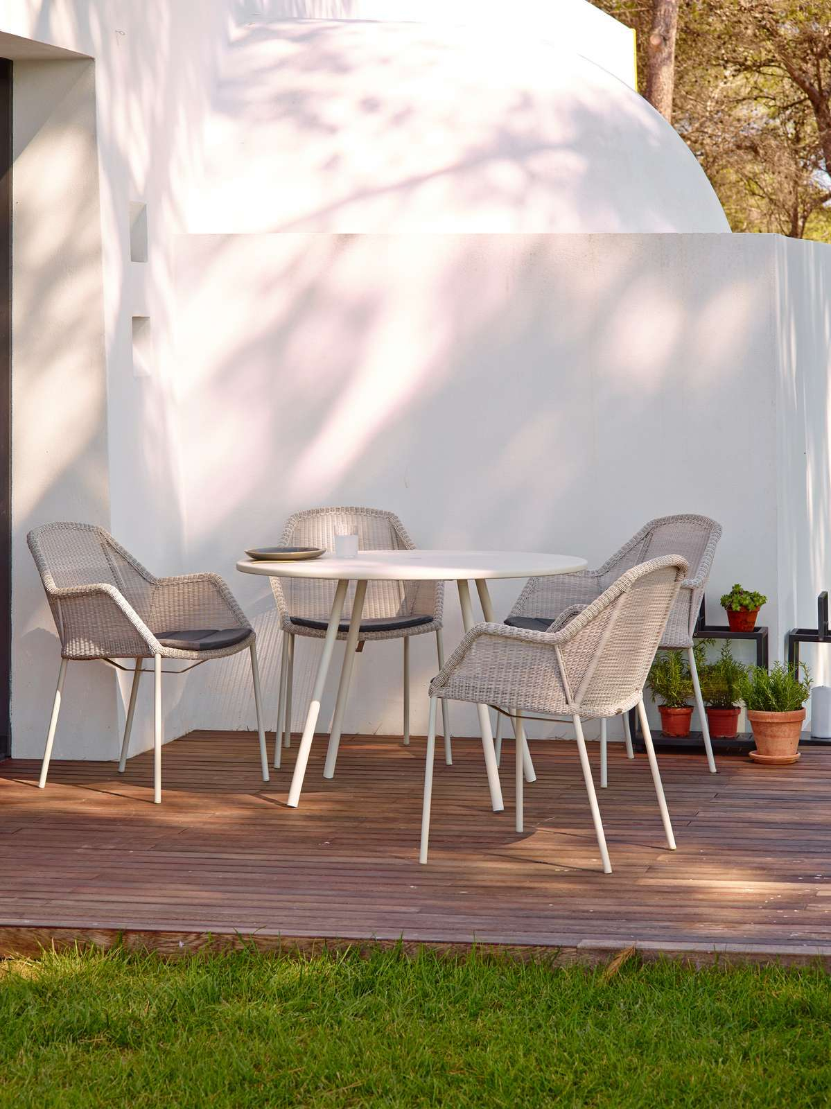 Breeze Outdoor Stühle von Cane-Line mit Vierfußgestell und grauem Geflecht um einen runden Gartentisch.