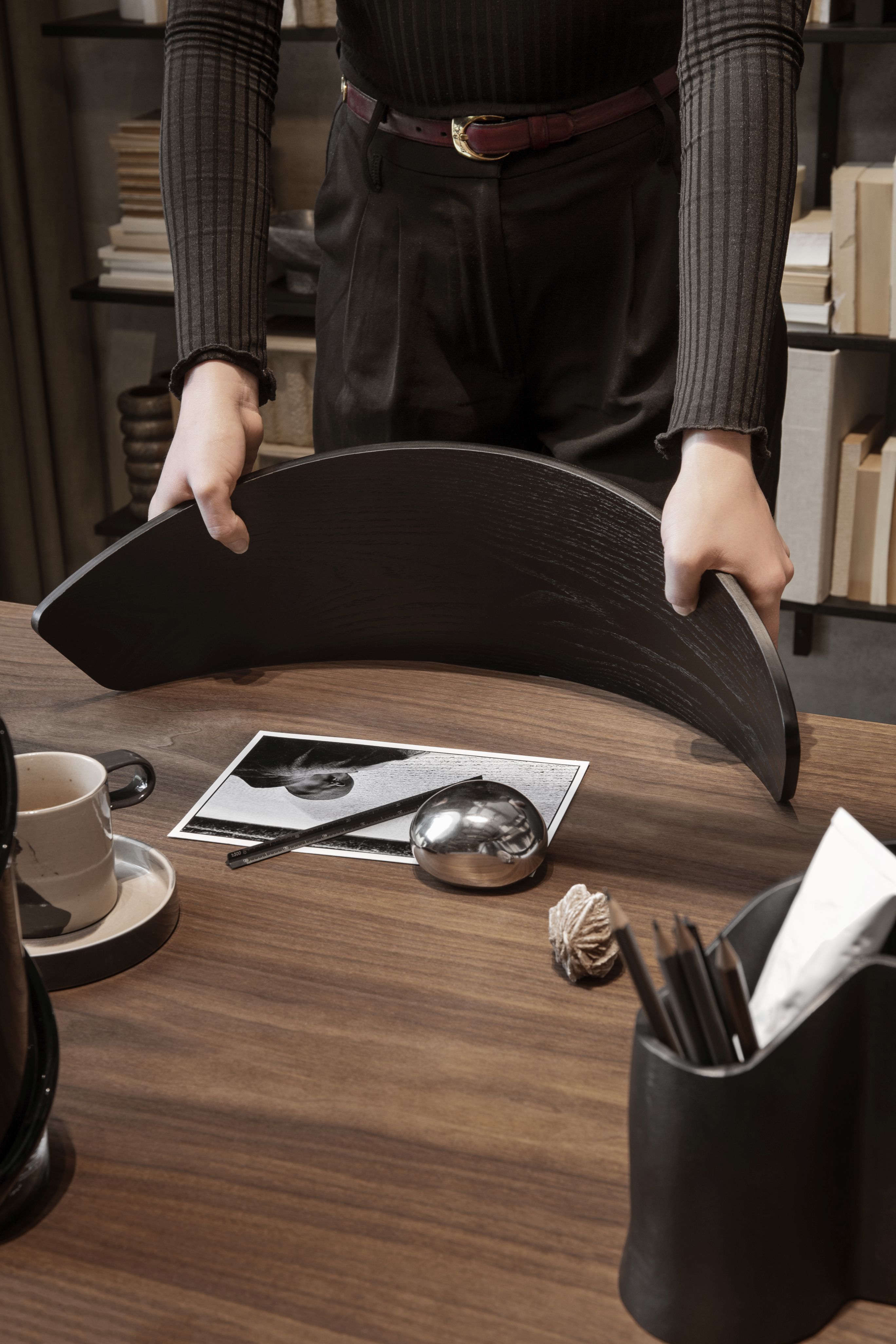 Nahaufnahme einer Person, die einen Herman Esszimmerstuhl von Ferm Living mit Holzgestell auf einen Schreibtisch legt.