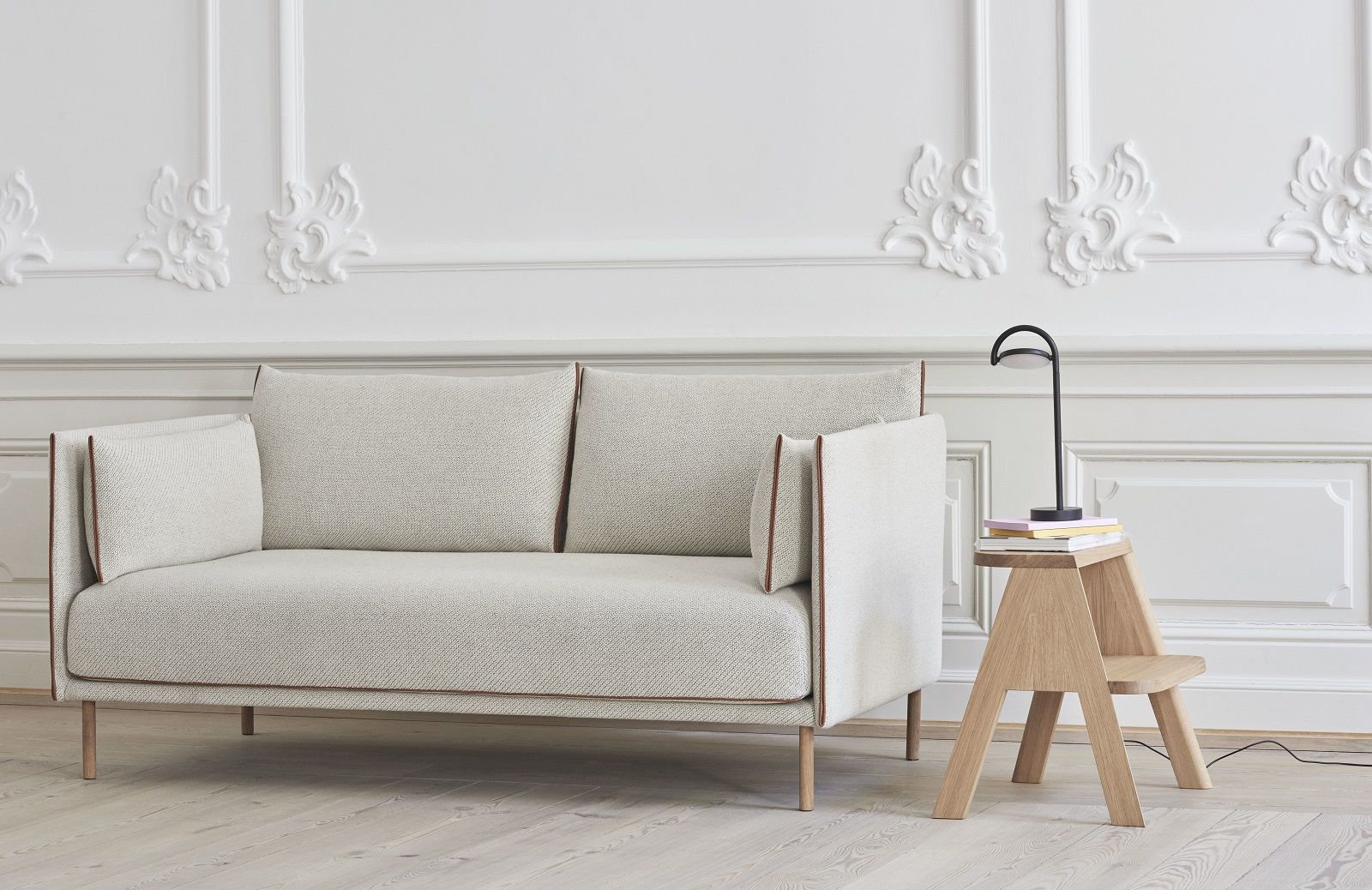 Silhouette Sofa 2-Sitzer Low Hay in hellem Stoff mit minimalistischem Design und Holztischlampe.