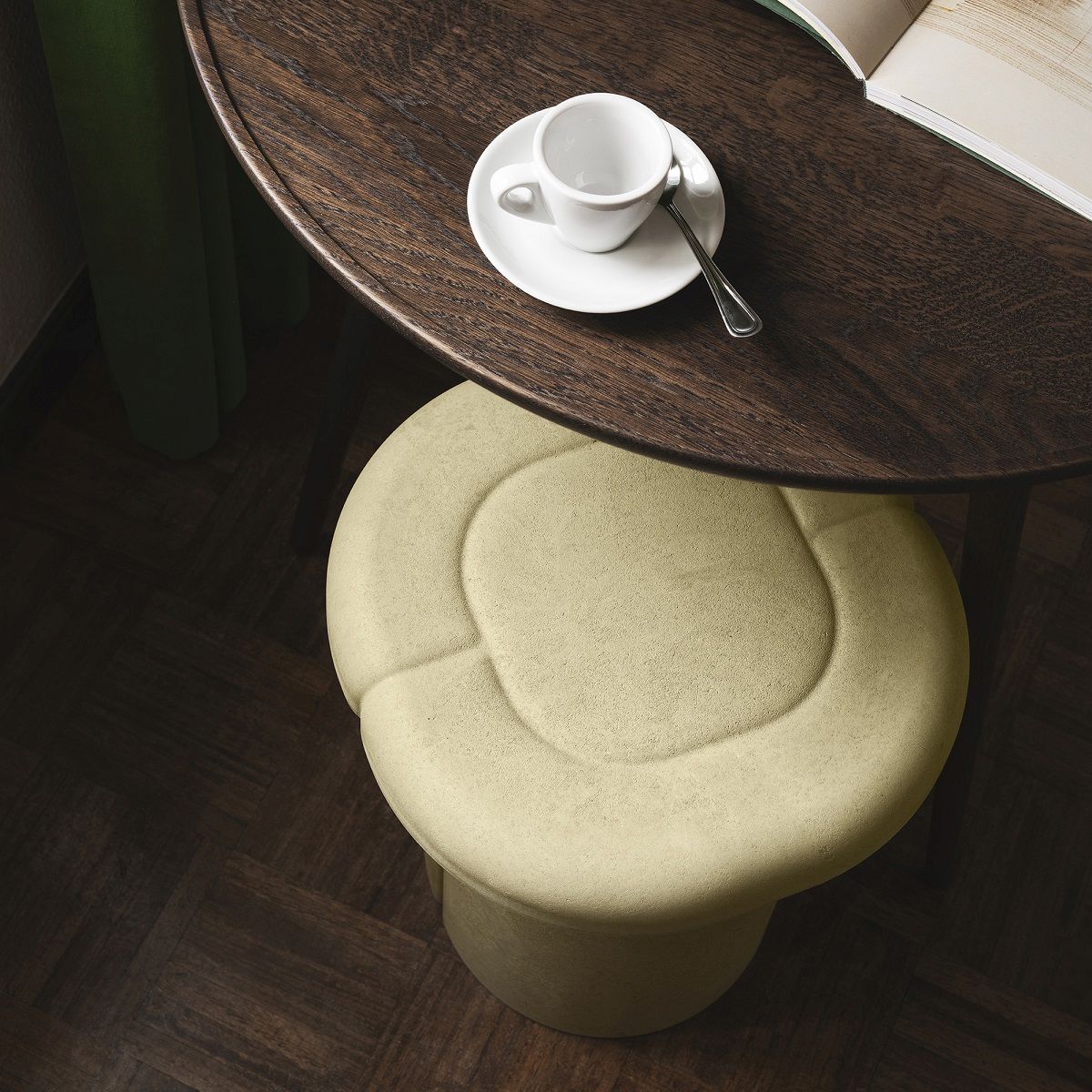Beiger Alder Stool Hocker von Mater unter einem dunklen Holztisch mit Kaffeetasse im Innenbereich.