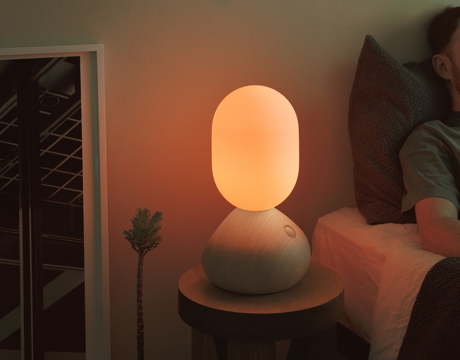 Sun Home Lichtskulptur Tischleuchte Grau auf Nachttisch mit warmem Licht neben schlafendem Mann im Bett.