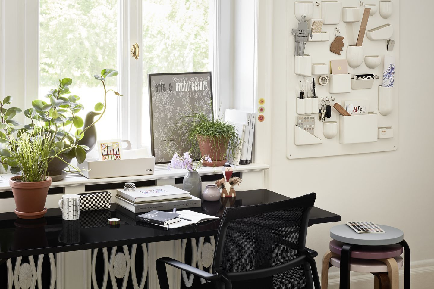 Detailaufnahme eines Schreibtisches mit Vitra Holzfigur, Pflanzen, Büchern und einem Wandorganizer im hellen Arbeitszimmer.