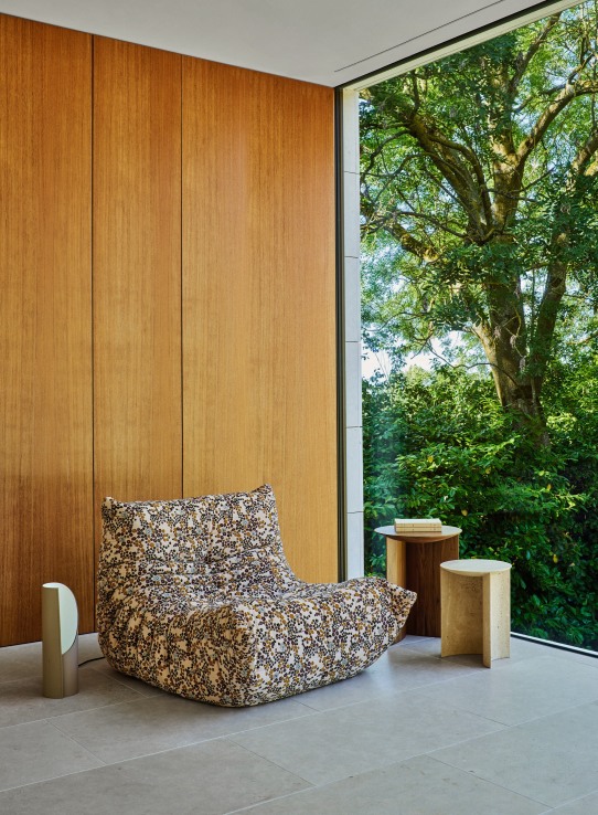 Gemusterter Togo Sessel von ligne roset im modernen Wohnzimmer mit Holzwand und Fensterblick.