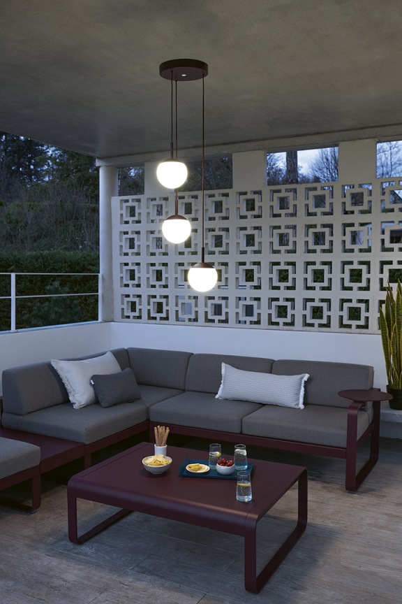 Mooon Triple Pendelleuchte von Fermob beleuchtet stilvoll eine Terrasse mit Lounge-Möbeln.