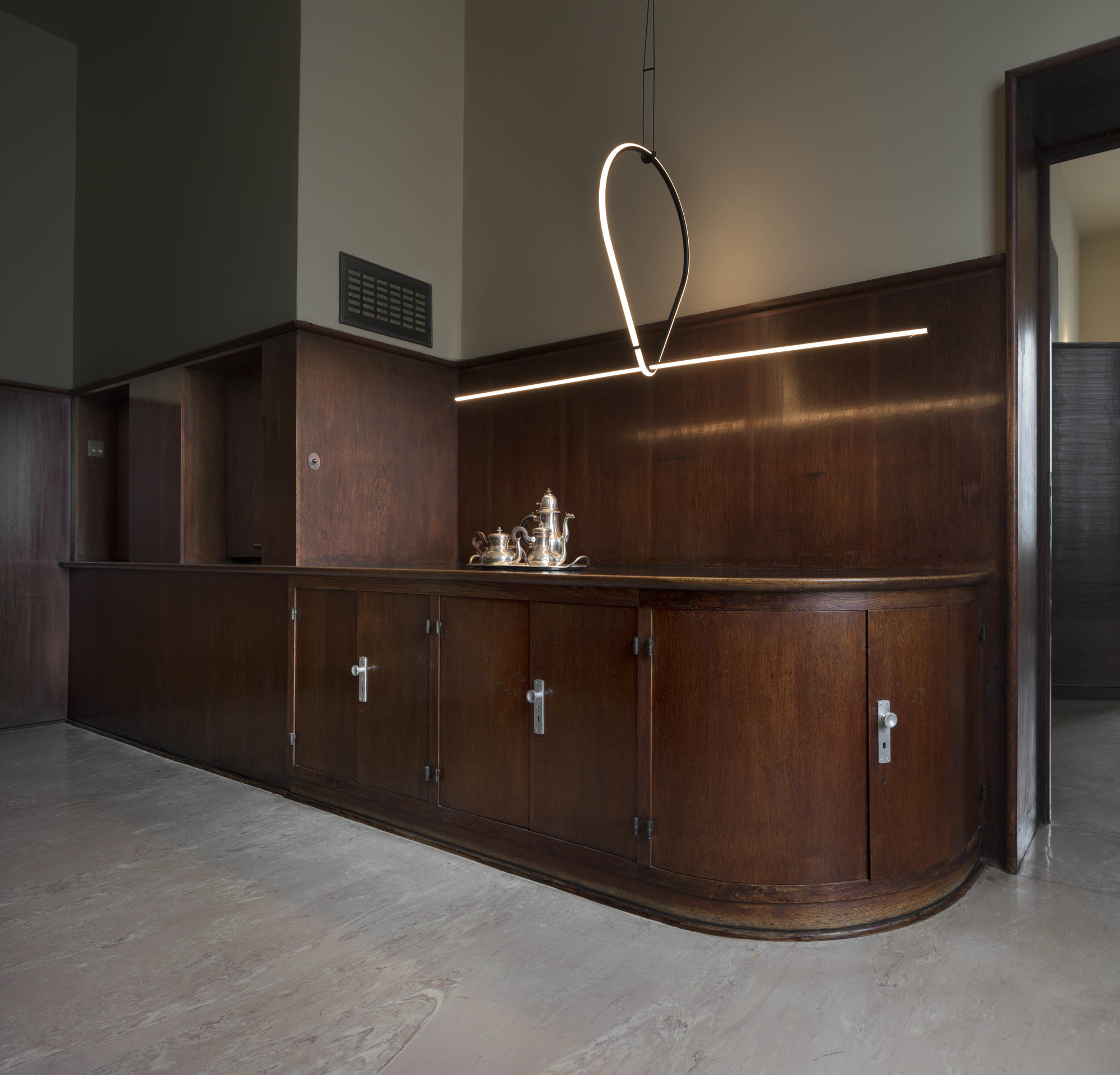 Moderne Flos Arrangements Pendelleuchte über einem dunklen Holzschrank mit Teegeschirr in einem stilvollen Interieur.