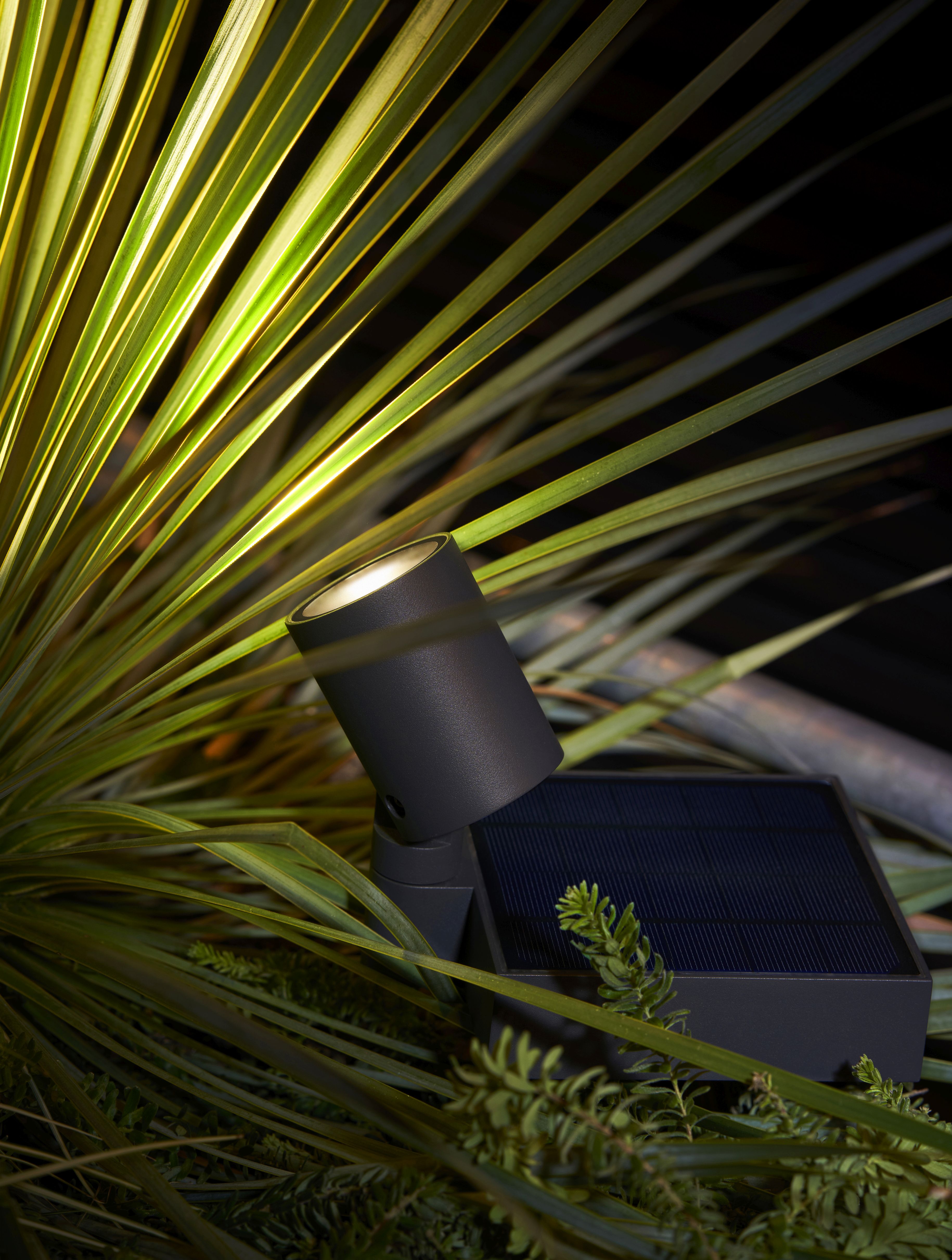 Moree Spot.E Solar-Gartenstrahler im Garten, umgeben von grünen Pflanzen, mit Solarpanel für umweltfreundliche Beleuchtung.