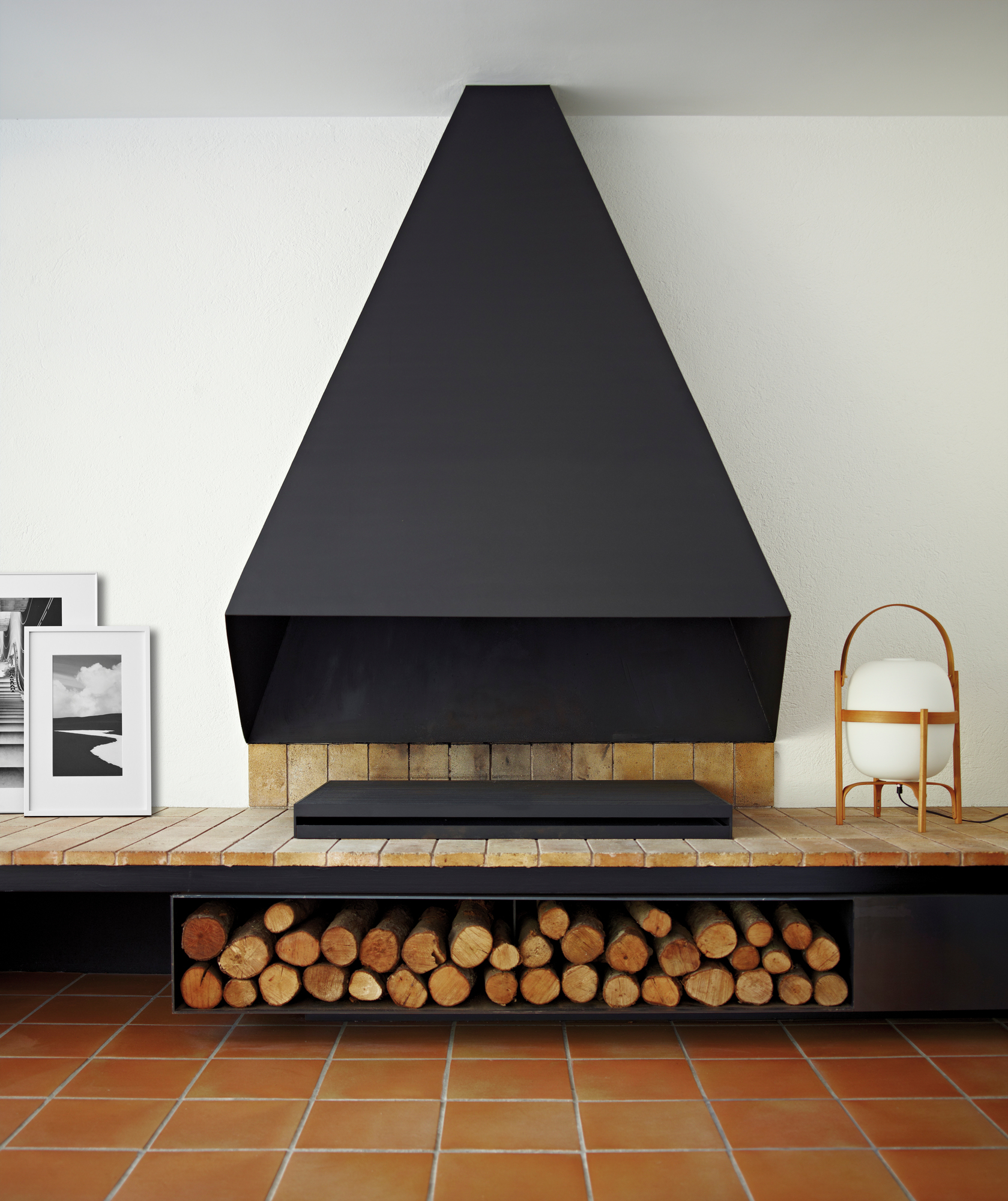 Cesta Tischleuchte von Santa & Cole als Nachttischlampe neben Kamin mit Holzscheiten im Wohnzimmer.