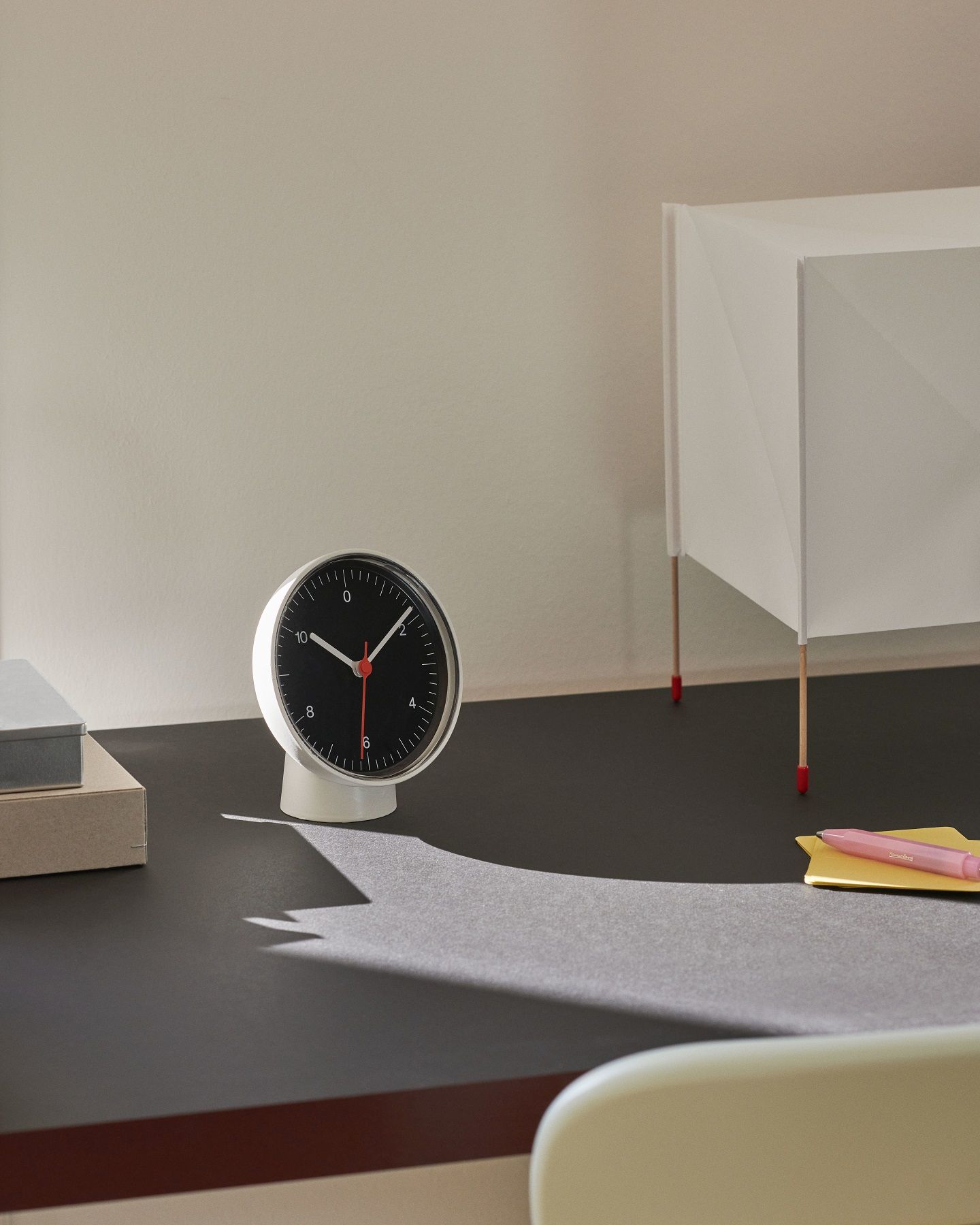 Hay Tischuhr/Wanduhr Dual-function in Weiß und Schwarz auf einem Schreibtisch mit Lampe und Notizen.