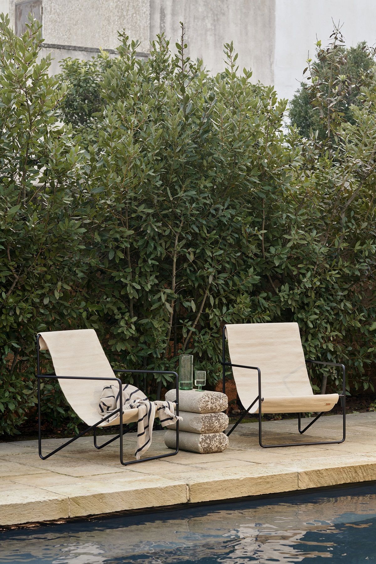 Zwei Desert Chair Loungesessel von Ferm Living im Garten, neben einem Pool, mit Handtuch.