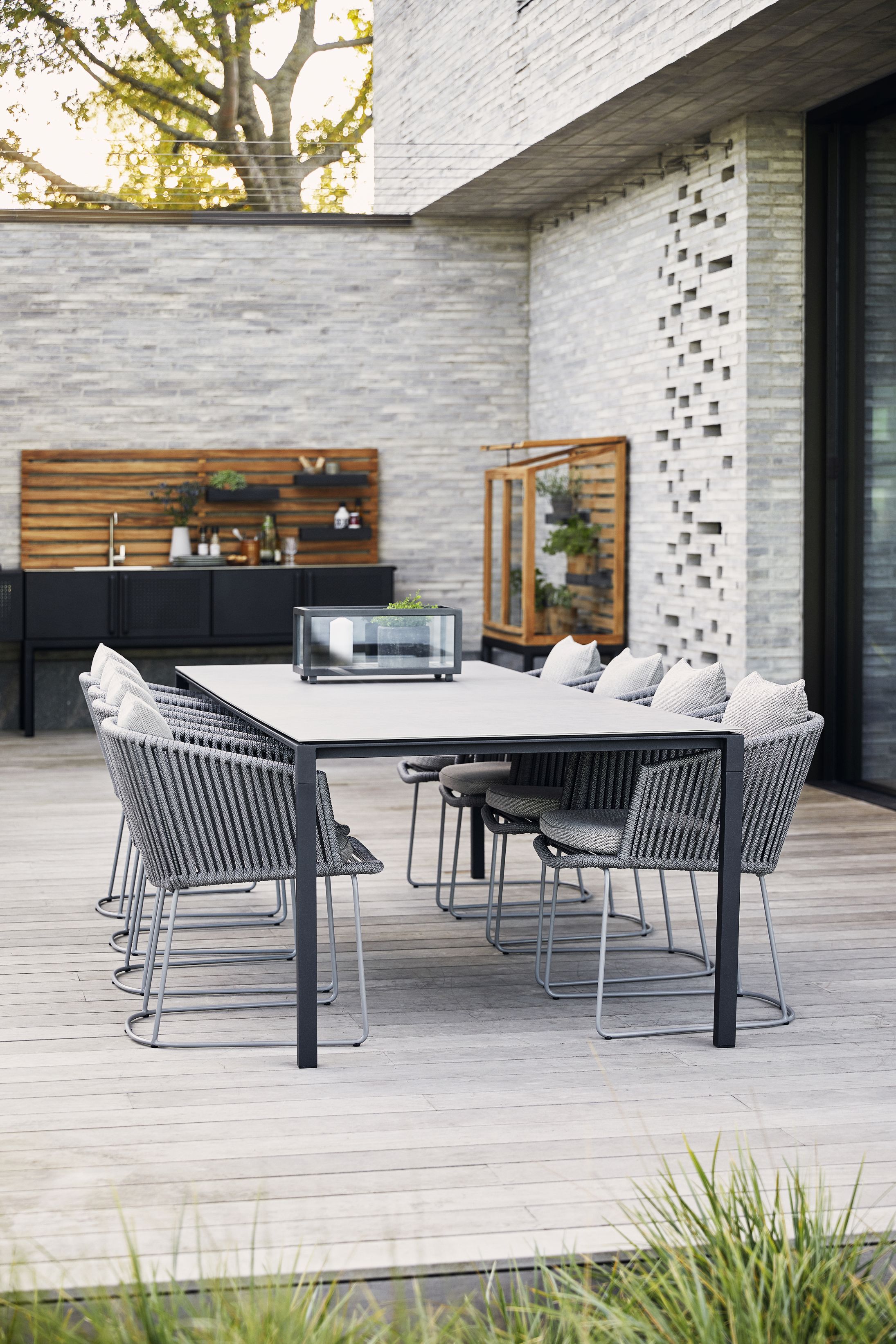 Großer Cane-Line Esstisch "Pure Outdoor" mit grauen Stühlen und Kissen auf einer Holzterrasse.