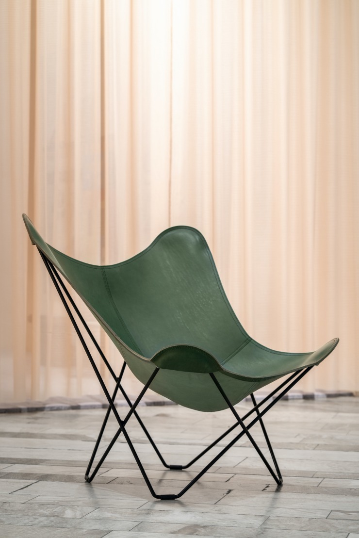Grüner Pampa Mariposa Butterfly Chair Ledersessel mit schwarzem Gestell vor hellem Vorhang.