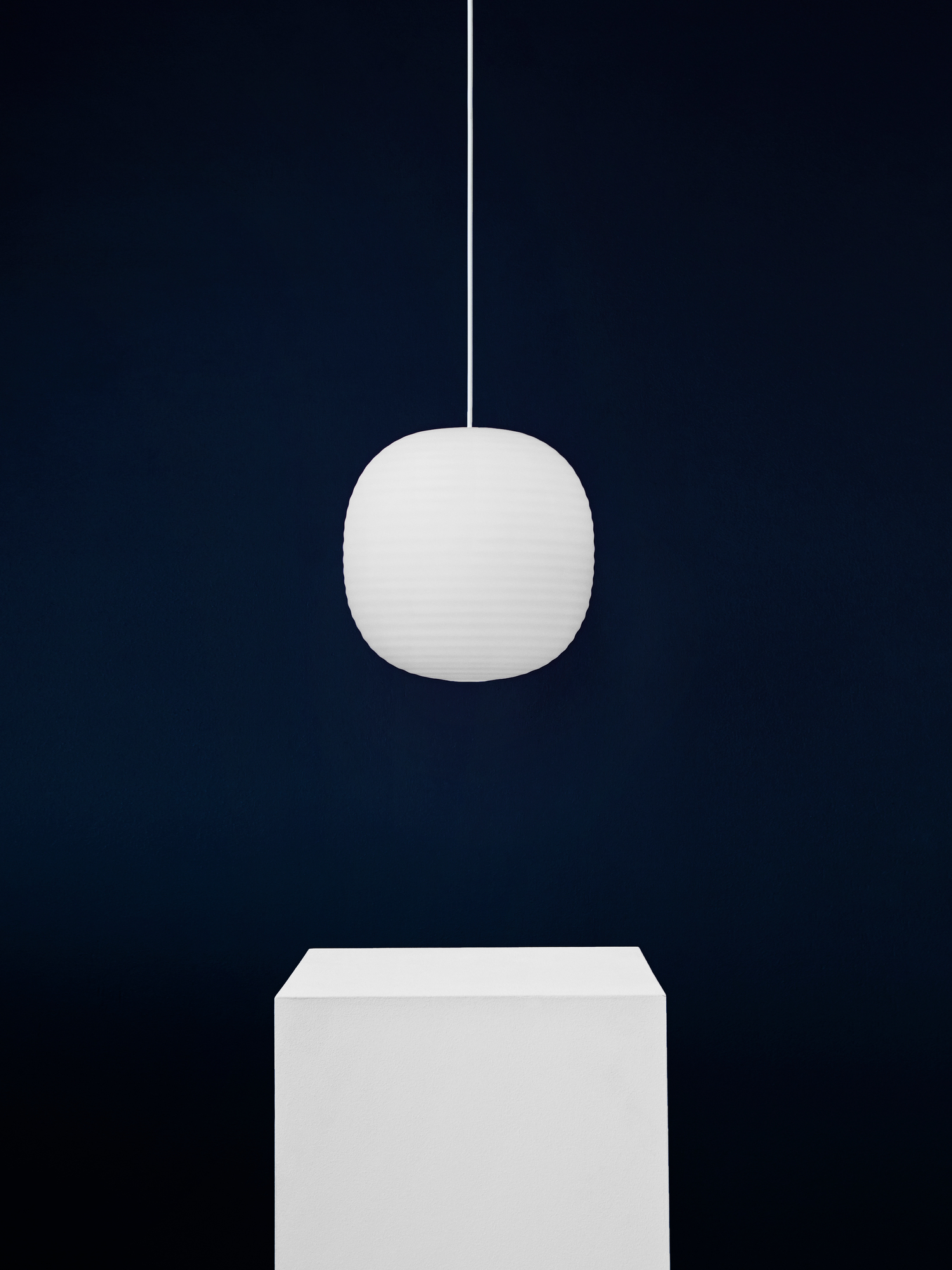 Weiße Lantern Pendant Pendelleuchte von New Works vor dunklem Hintergrund, moderne Hängelampe für Wohnraumbeleuchtung.