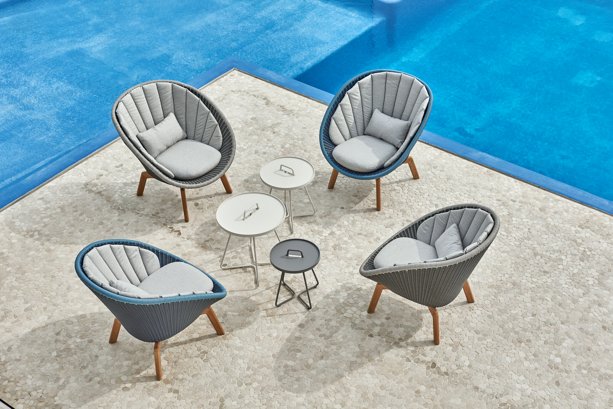 Draufsicht: Vier Cane-Line Peacock Loungesessel aus Rattan mit Kissen und Beistelltischen am Pool.