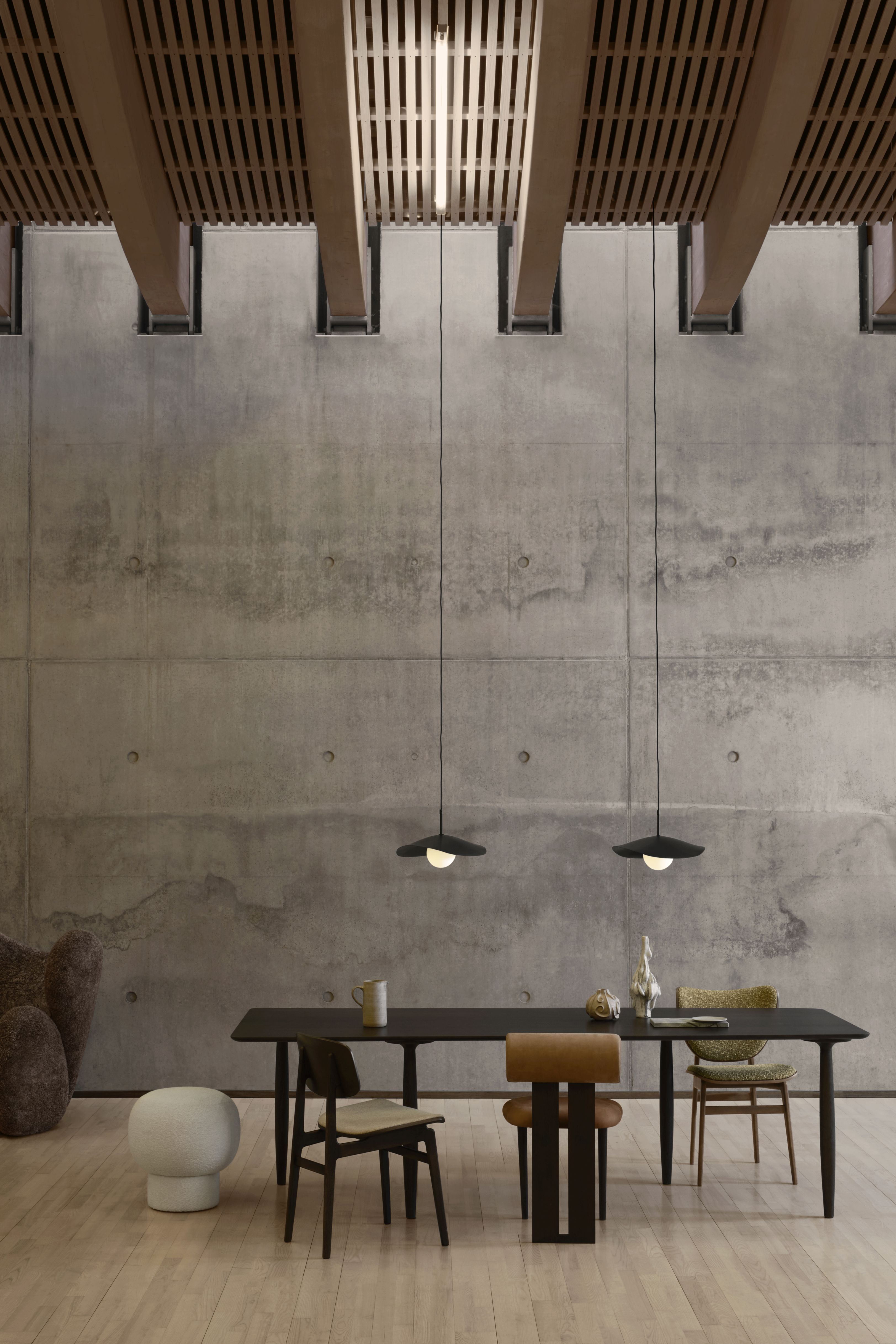 Fuji Pendelleuchte von Norr11 über Esstisch mit Stühlen, moderne Innenarchitektur mit Betonwand und Holzdecke.