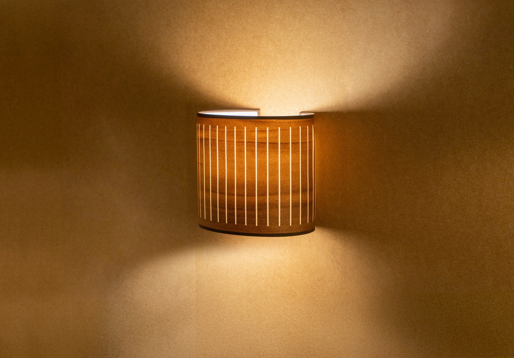 Nahaufnahme der beleuchteten Autumn Wall Wandleuchte von nomon  mit Holzlamellen an einer Wand.