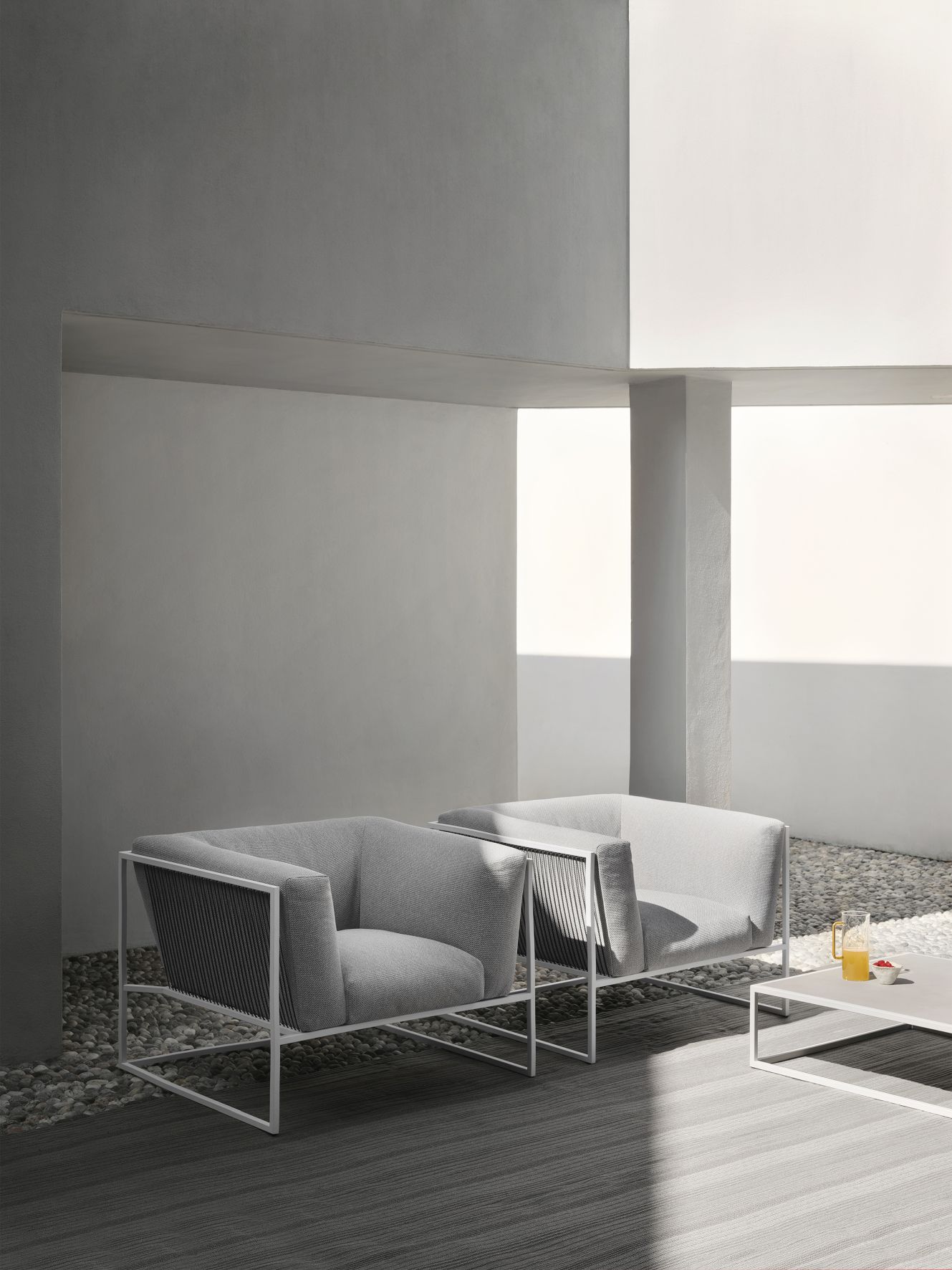 Zwei graue Arpa Outdoor Sessel von MDF Italia mit weißem Rahmen auf einer Terrasse.