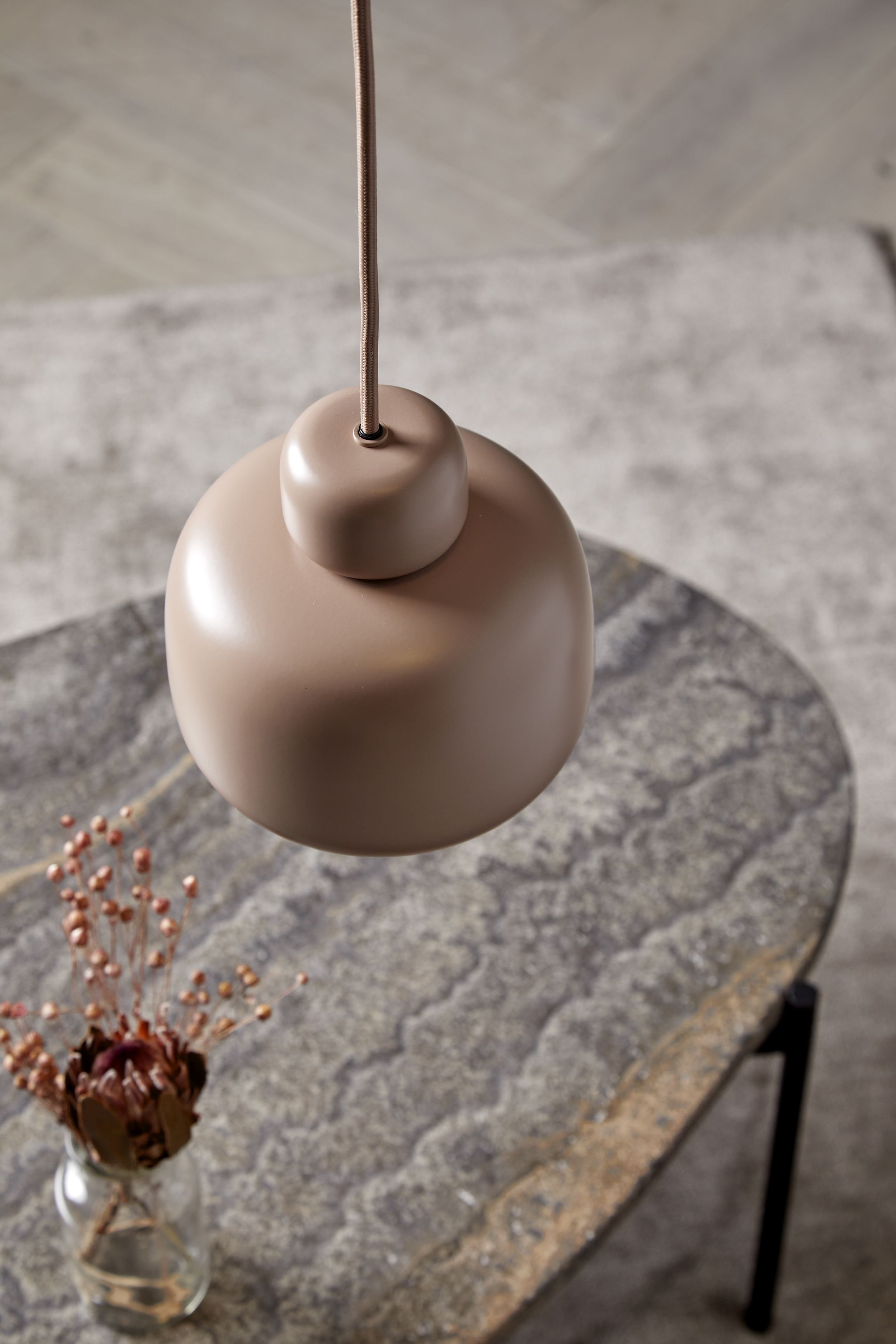 Nahaufnahme der kleinen Woud Stone Pendant Pendelleuchte in Beige, hängend über einem Steintisch.