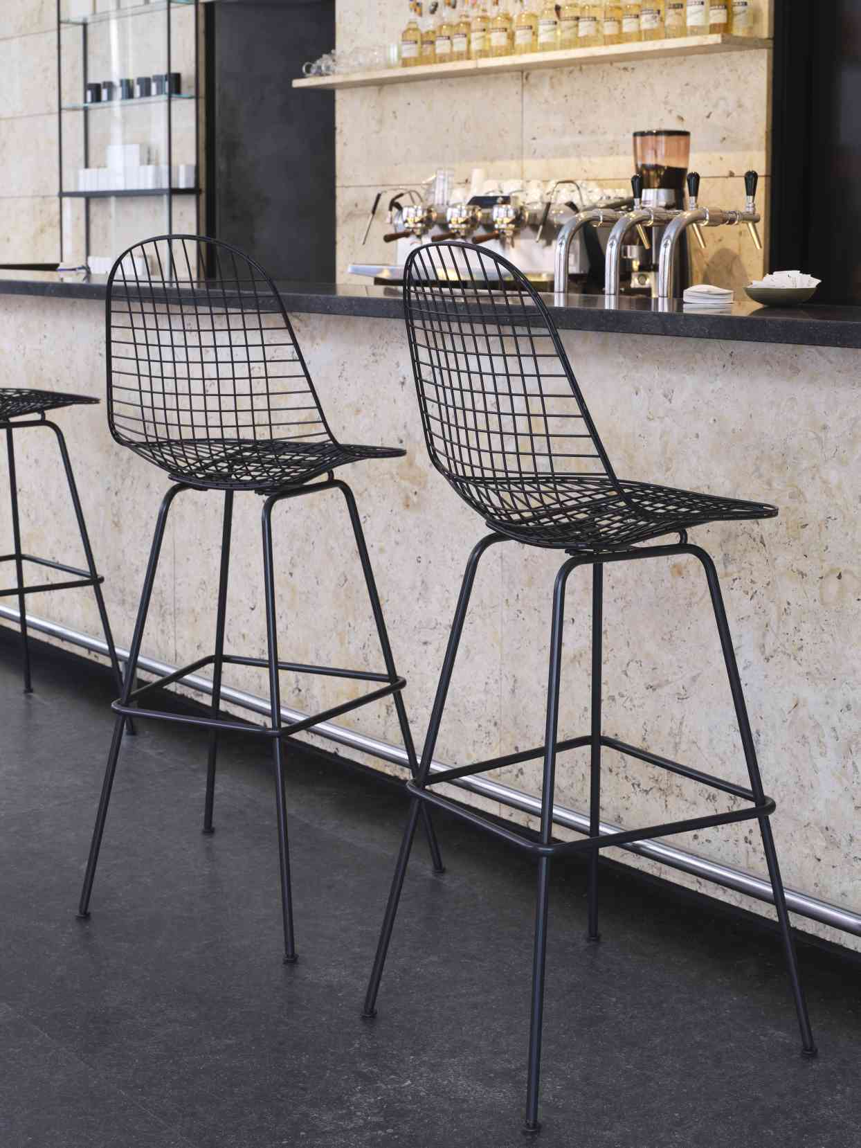 Schwarzer Eames Wire Bar Stool Barhocker von Vitra vor einer Bar, modernes Design.