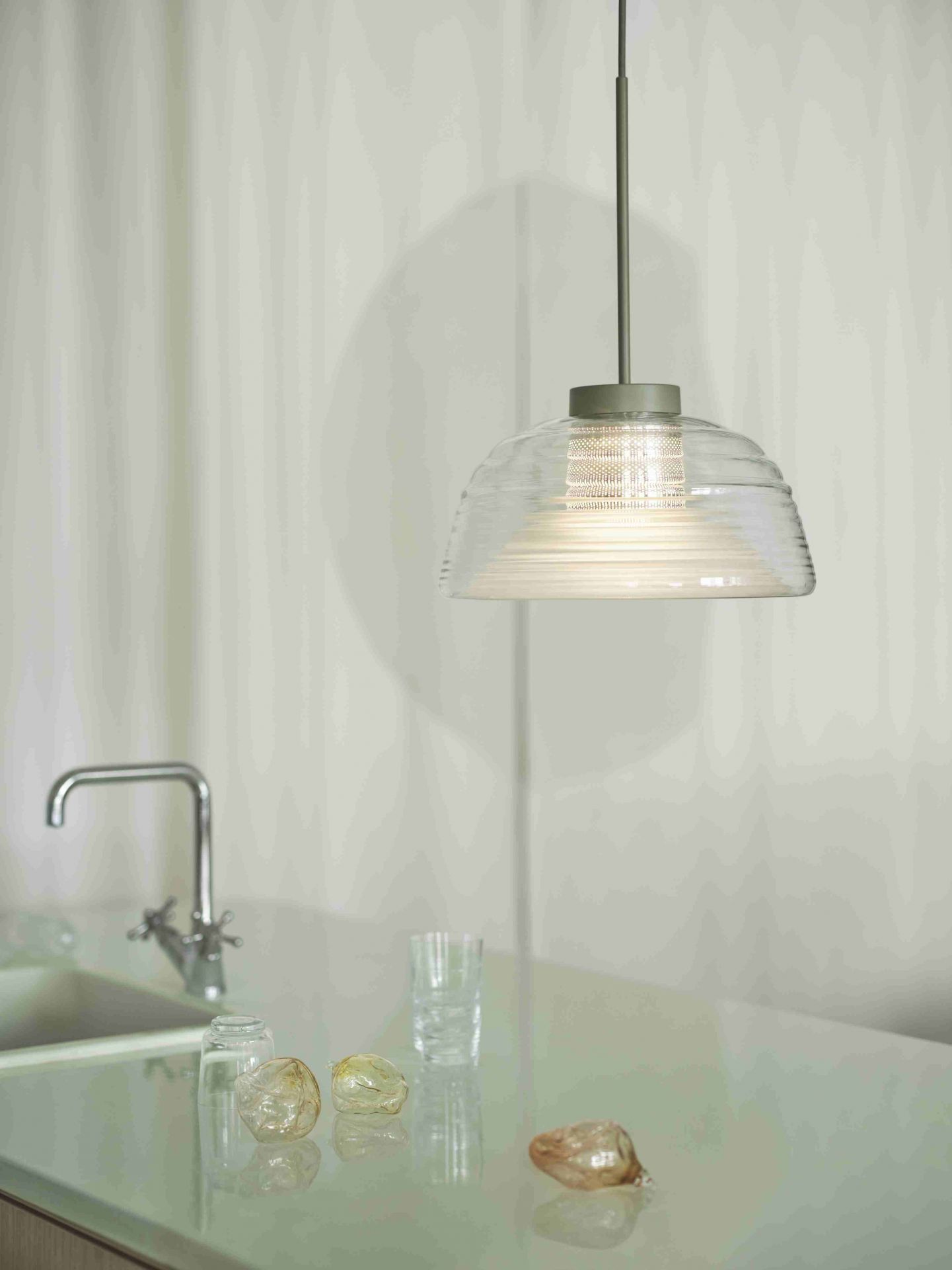 Moderne Hängelampe aus Glas über einer Küchenzeile mit Armatur und Gläsern, stimmungsvolle Beleuchtung.