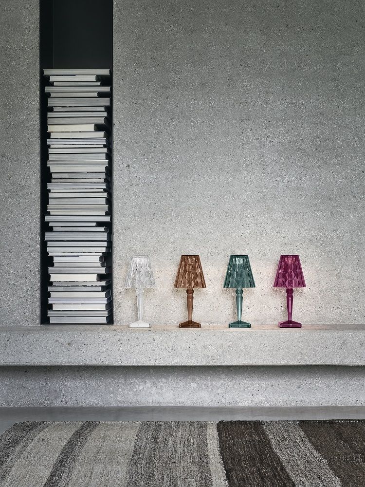 Vier farbige Big Battery Tischleuchten von Kartell auf einem Regal vor einer grauen Wand.