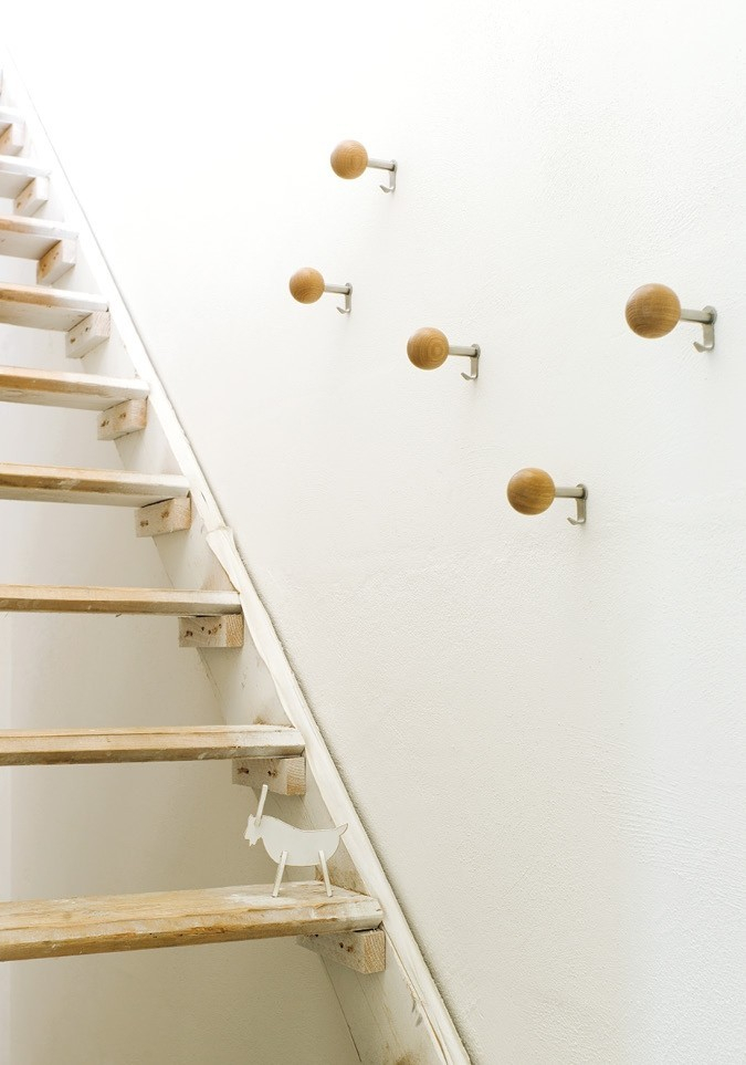 Fünf Schönbuch Dots Mantelhaken aus Holz und Metall an einer weißen Wand neben einer Treppe.