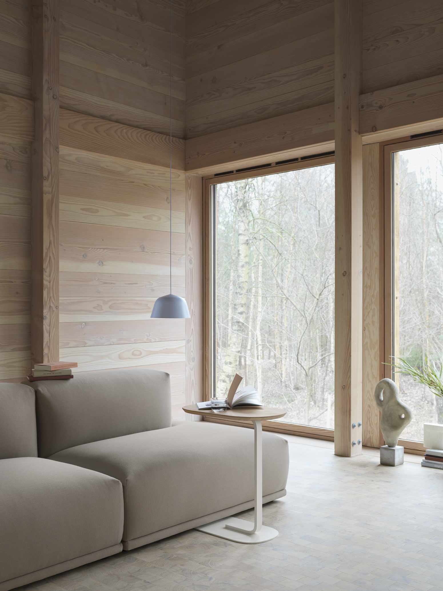 Helle, moderne Inneneinrichtung mit grauer Ambit Pendelleuchte von Muuto über einem Sofa und Beistelltisch.