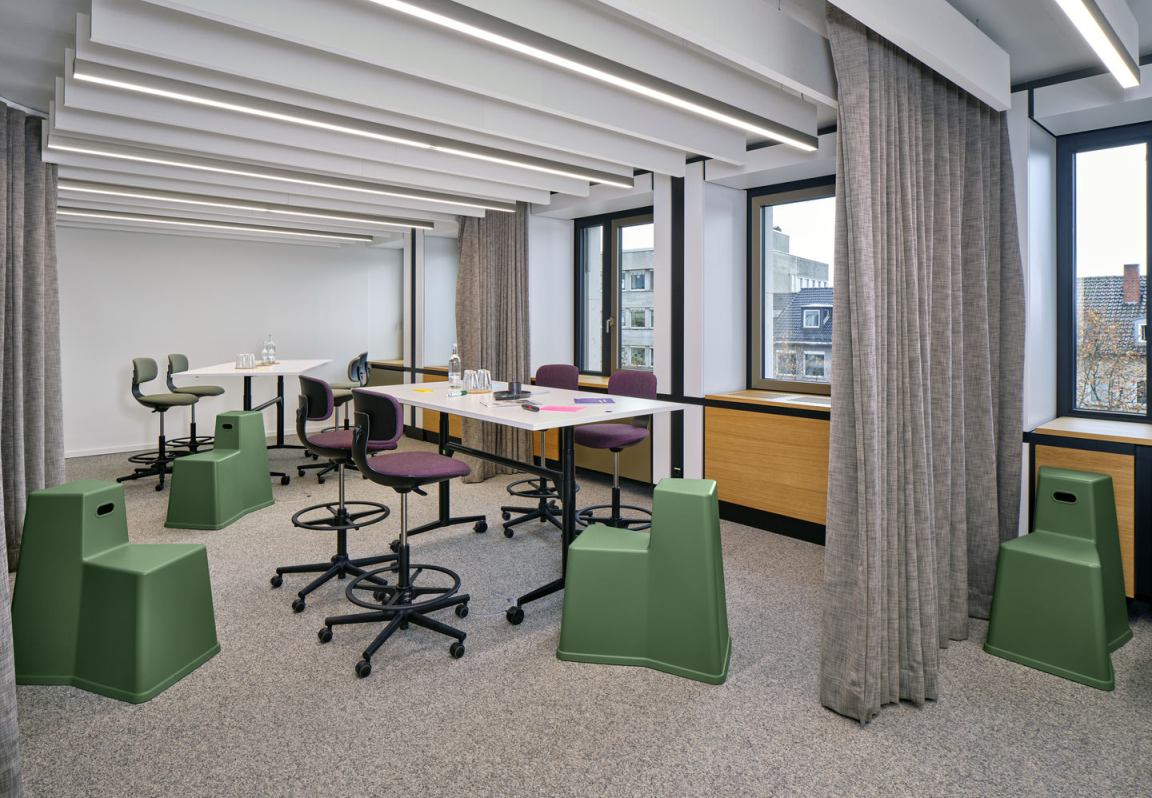 Besprechungsraum mit Vitra Rookie High Drehstühlen in Lila und grünen Hockern an weißen Tischen.