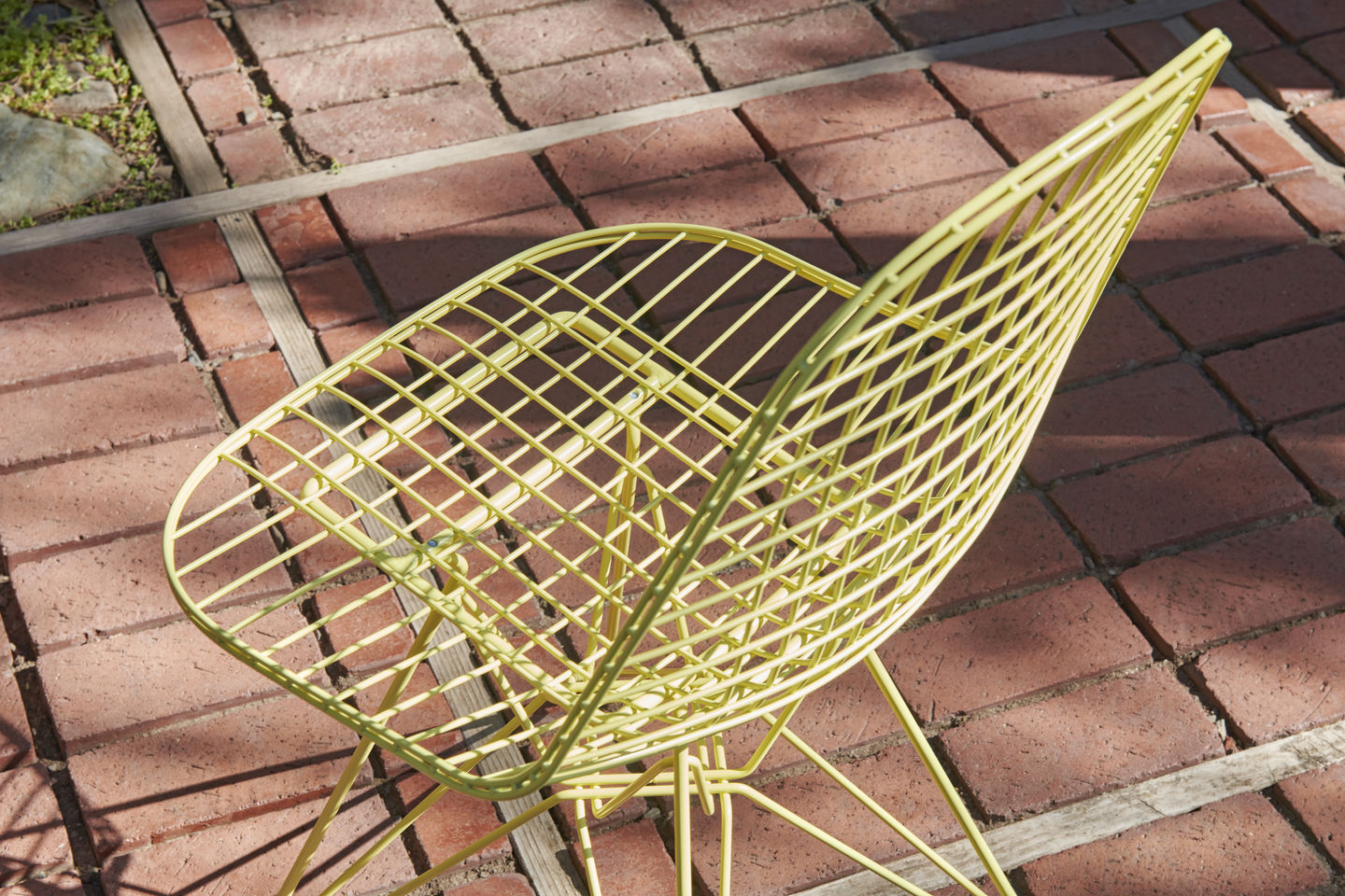 Nahaufnahme des gelben Vitra DKR Wire Chair Stuhls ohne Polsterung auf einem Backsteinboden.