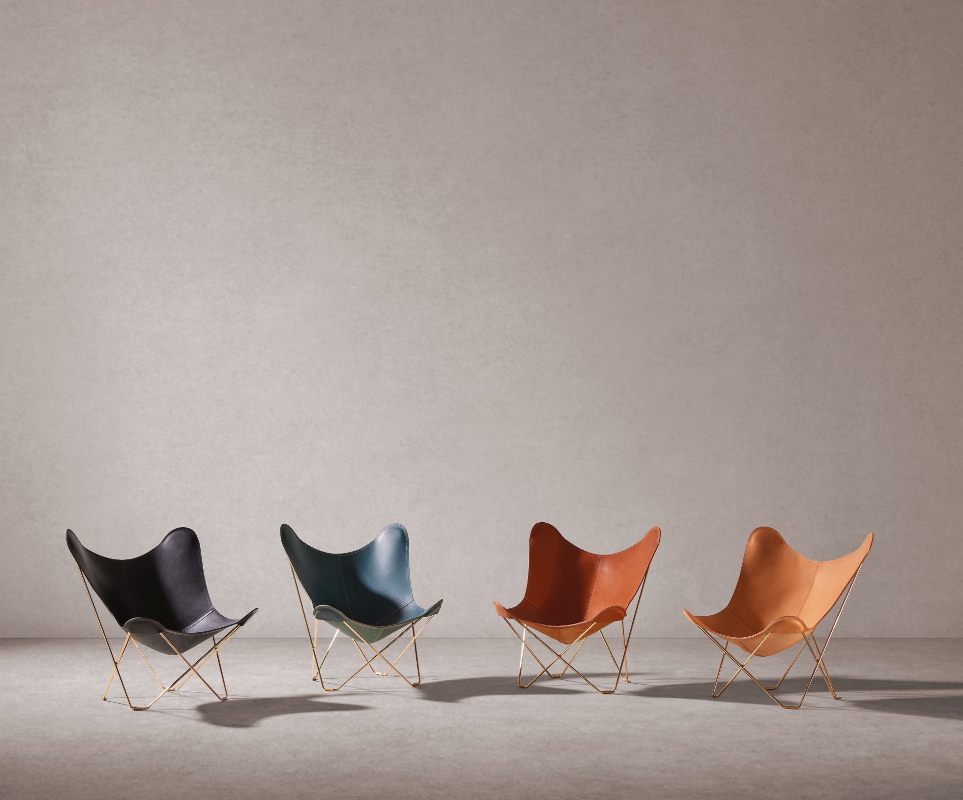 Vier Ledersessel im Butterfly-Design in Schwarz, Blau, Orange und Hellbraun mit goldenem Metallgestell.