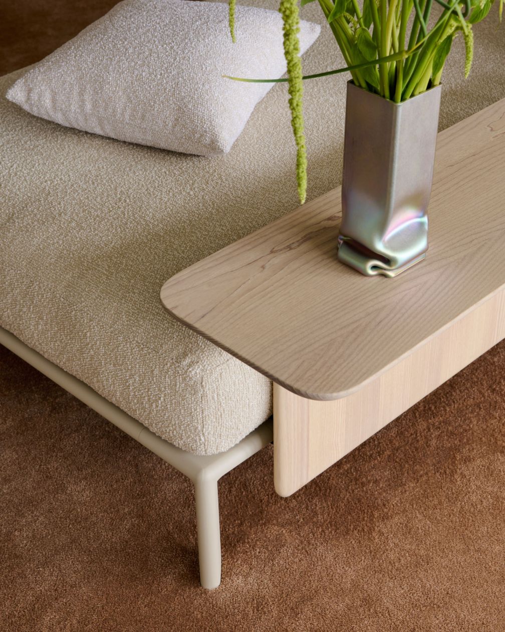 Nahaufnahme einer modernen Tagesliege mit beigem Kissen und Holztisch mit dekorativer Vase.