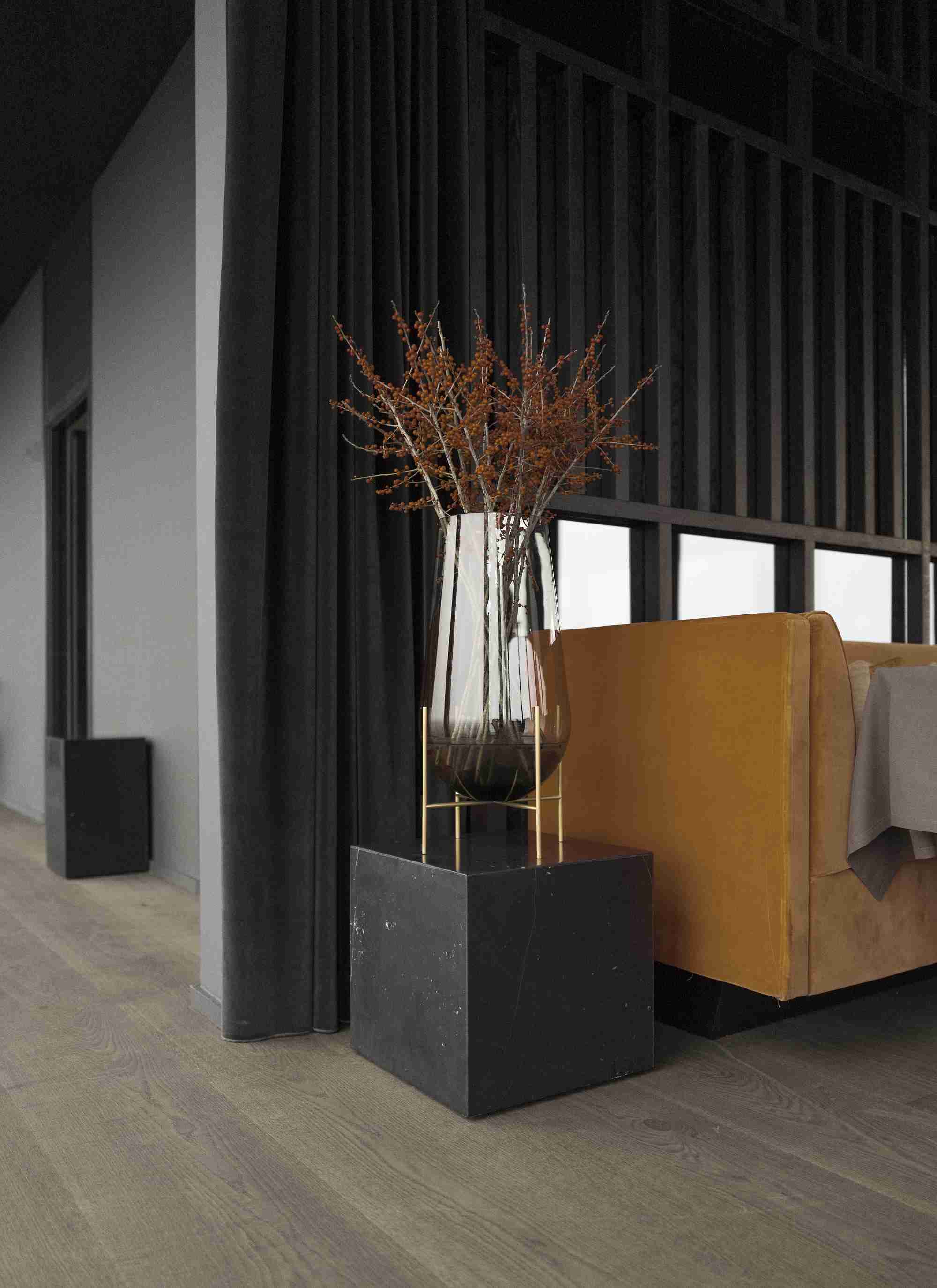 Audo Copenhagen Plinth Tisch aus Marmor mit Glasvase und Zweigen im modernen Wohnzimmer.