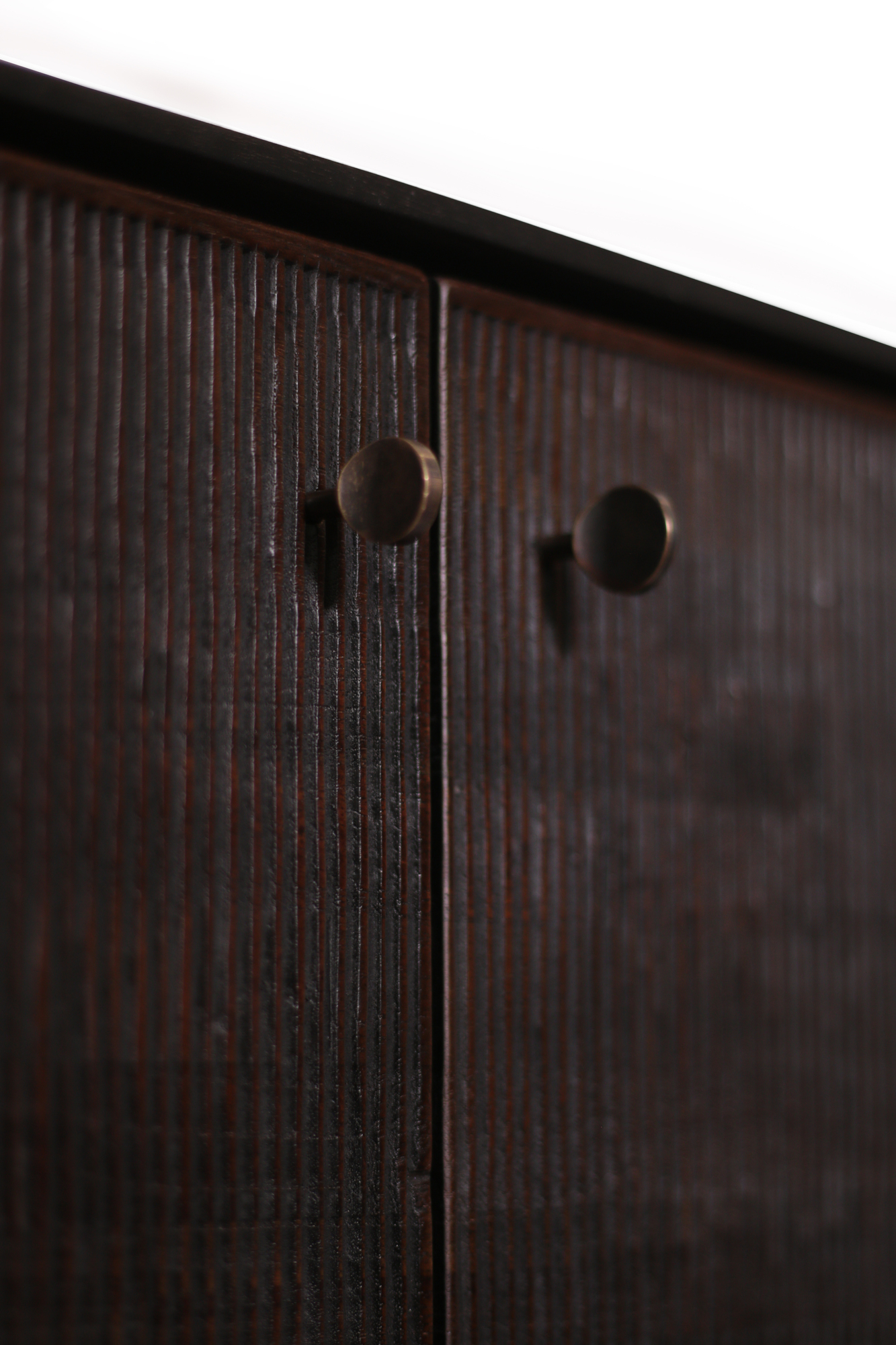 Detailaufnahme der Ethnicraft Teak Grooves Anrichte mit dunklem Holz und zwei runden bronzefarbenen Griffen.