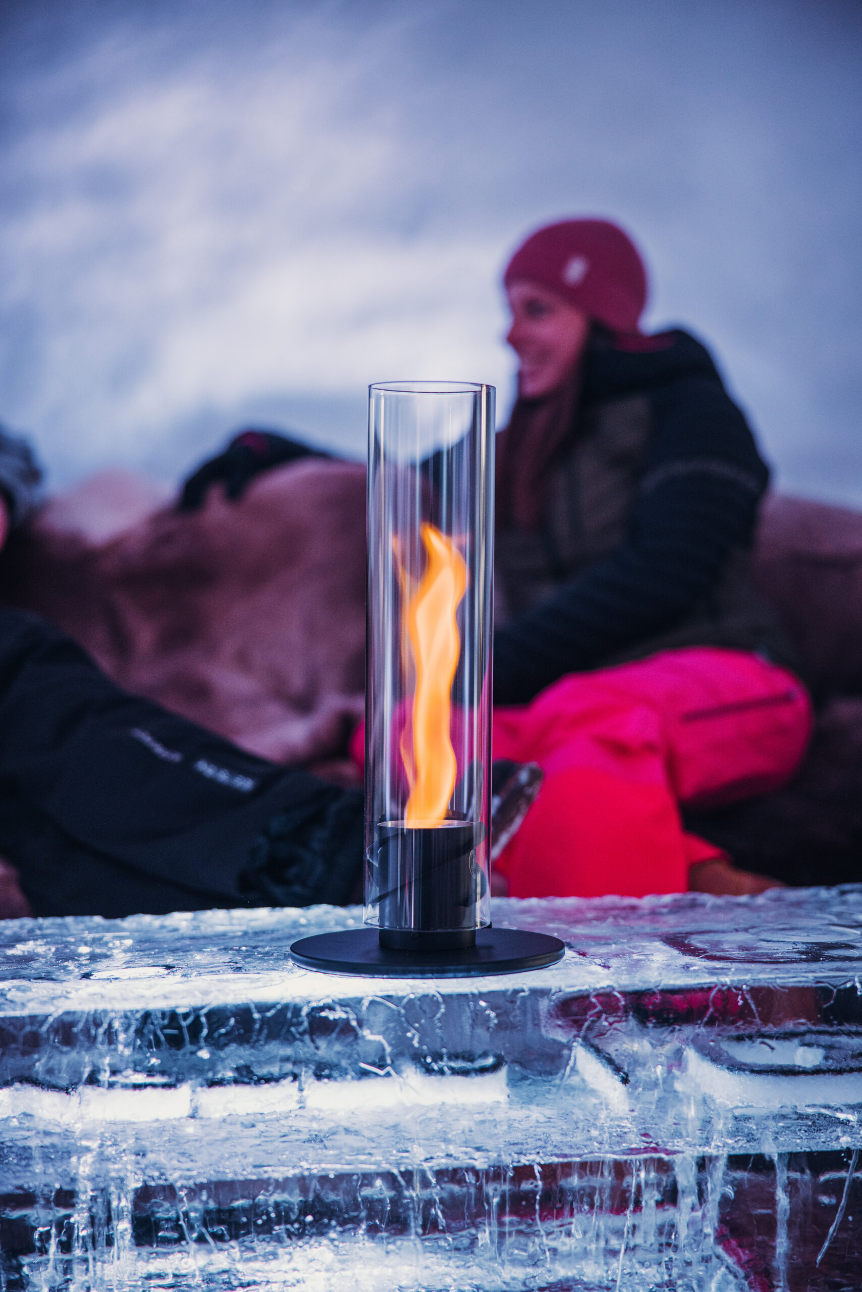 Moderner Tischkamin mit Glaszylinder und Flamme auf Eistisch, für stimmungsvolle Atmosphäre im Winter.