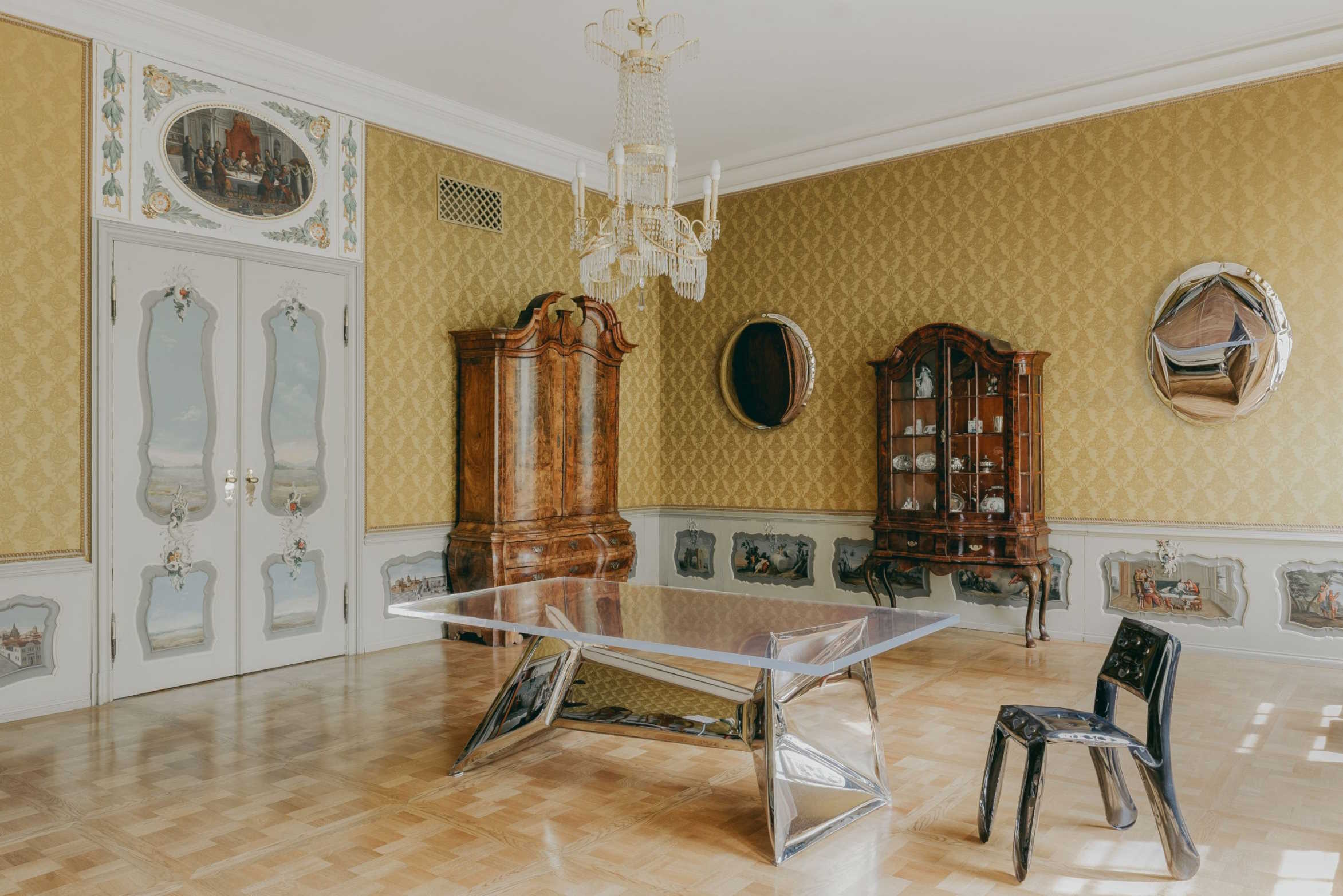 Klares Acryl Tisch mit Chrombeinen und schwarzer Stuhl in einem opulenten, historischen Raum.