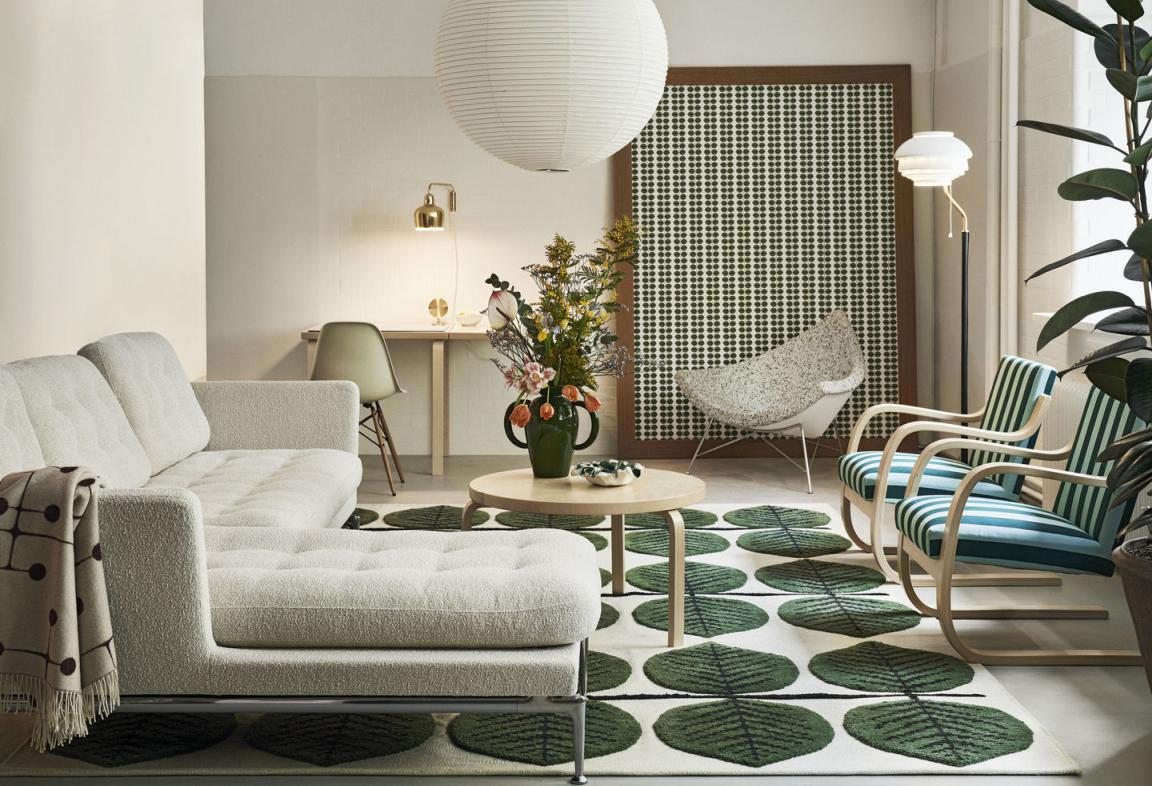 Helle Wohnzimmer-Szene mit Vitra Coconut Chair, Sofa, Teppich mit Blattmuster, Tisch mit Blumen und Stehlampe.