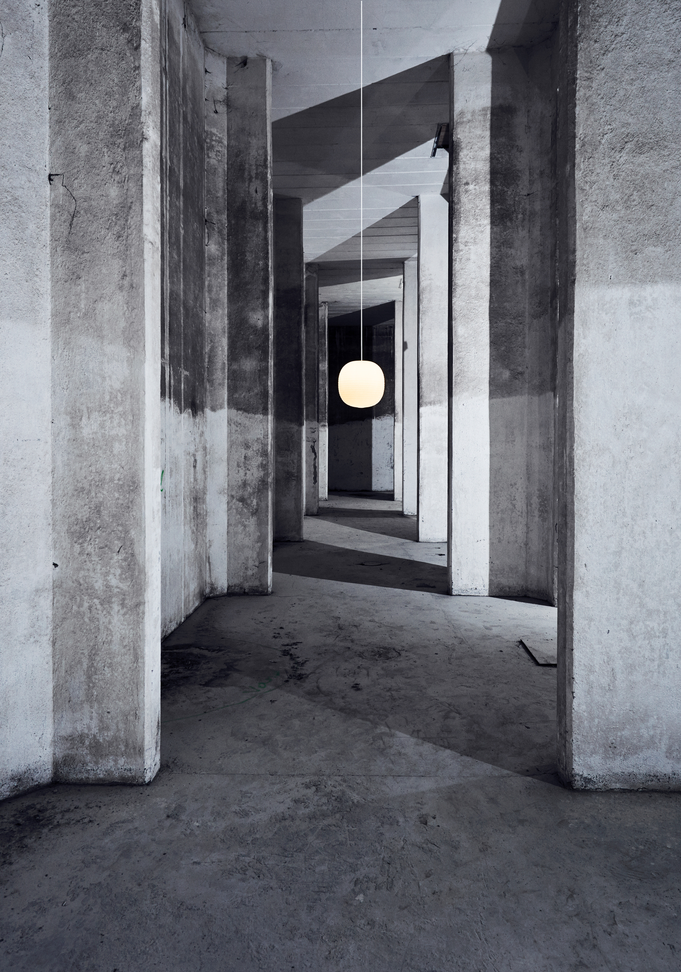 New Works Lantern Pendelleuchte, eine moderne, kugelförmige Hängelampe in einem industriellen Betonkorridor.