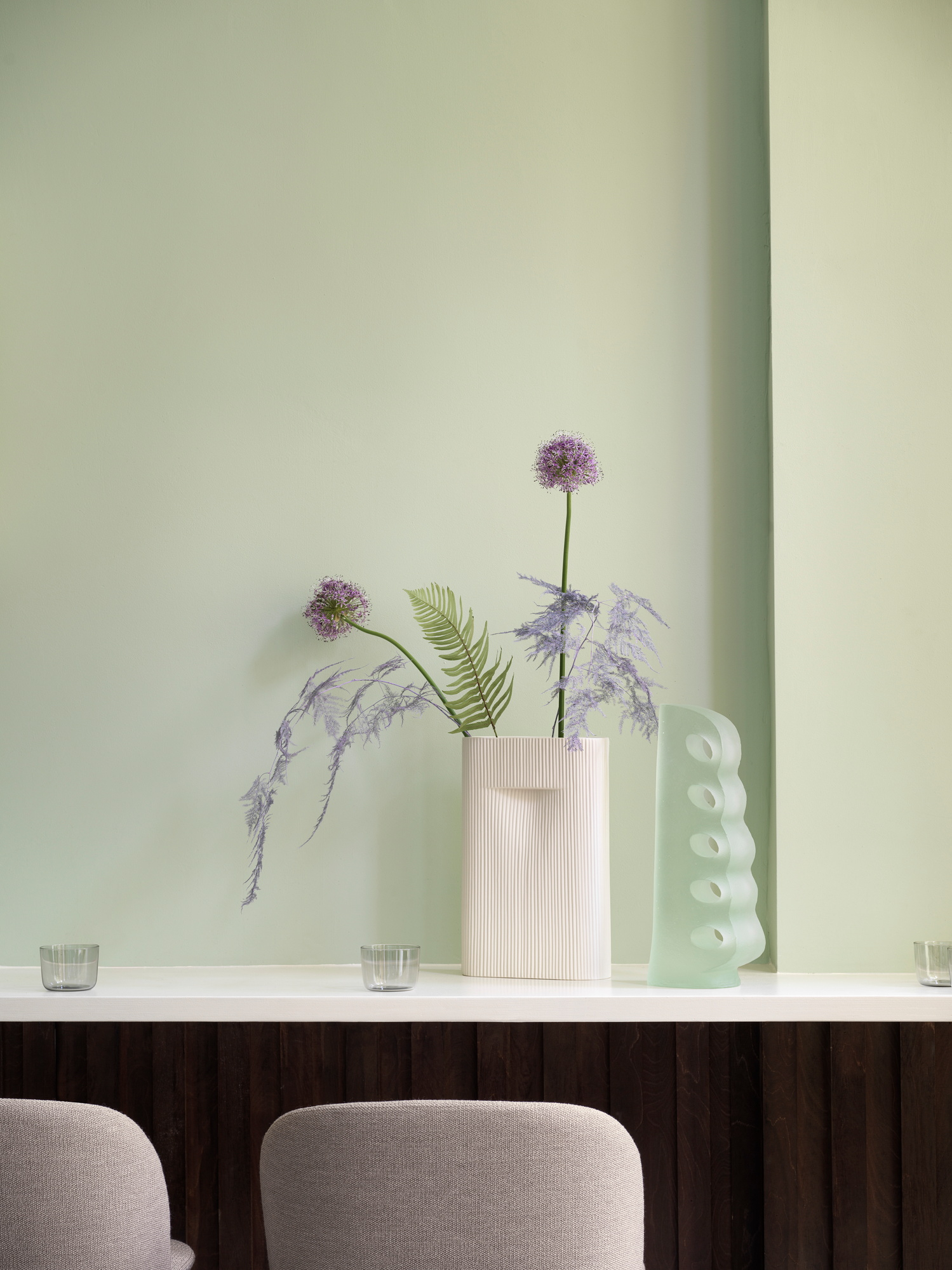 Muuto Oslo Barhocker in Grau vor einer mintgrünen Wand mit dekorativen Vasen.