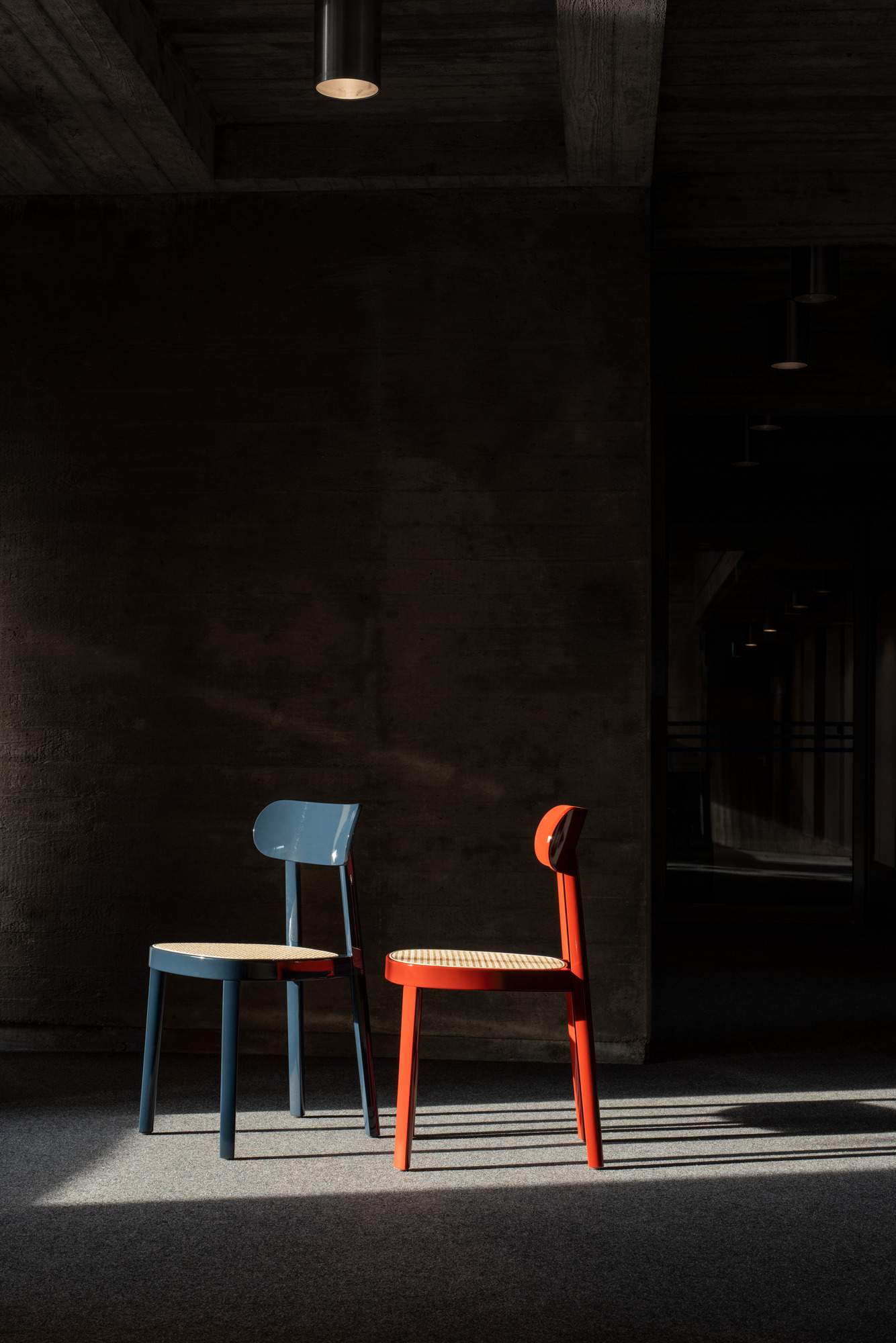 Blauer und roter Holzstuhl Thonet 118 mit Wiener Geflecht Sitzfläche vor dunklem Hintergrund.