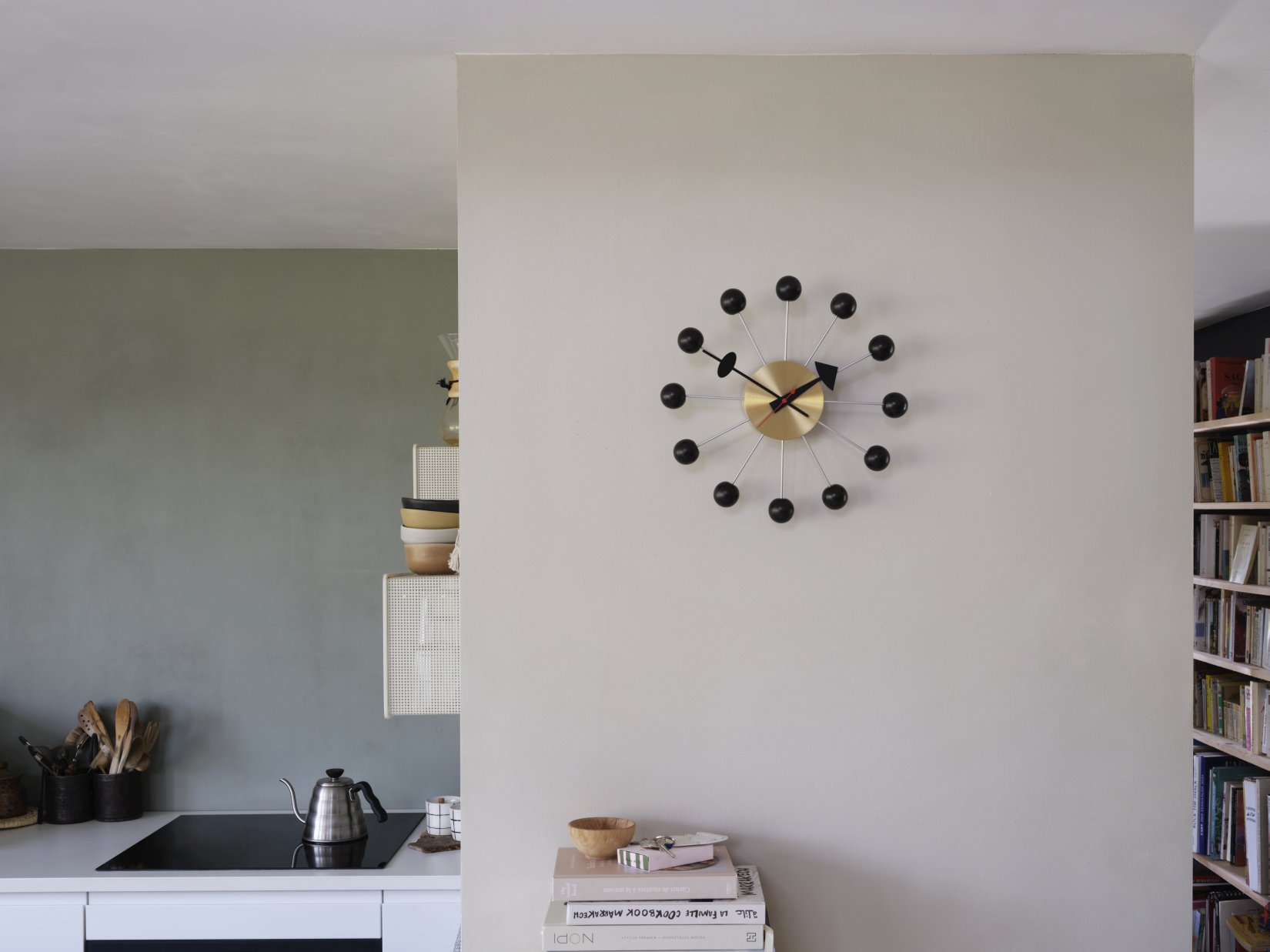 Moderne Wanduhr im Atomic Design mit goldenem Zifferblatt und schwarzen Kugeln im Küchenambiente.