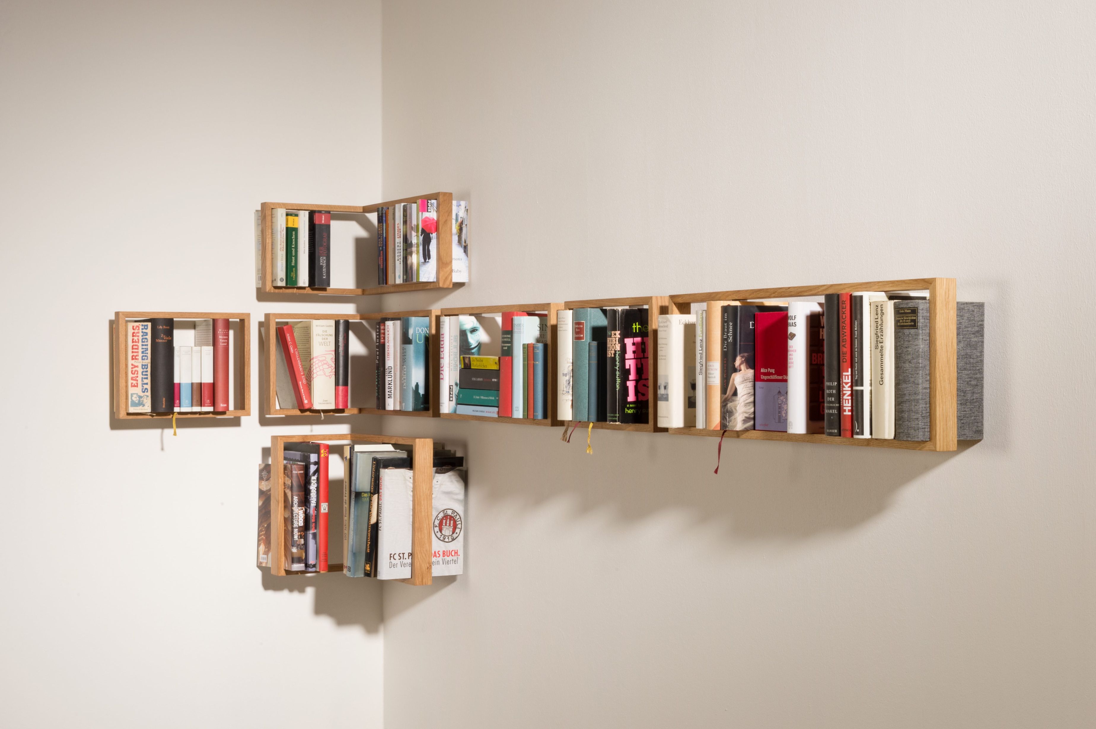 Wandmontiertes Regal b Eiche, bestehend aus mehreren kleinen Holzregalen, gefüllt mit Büchern, modernes Design, Unikat.