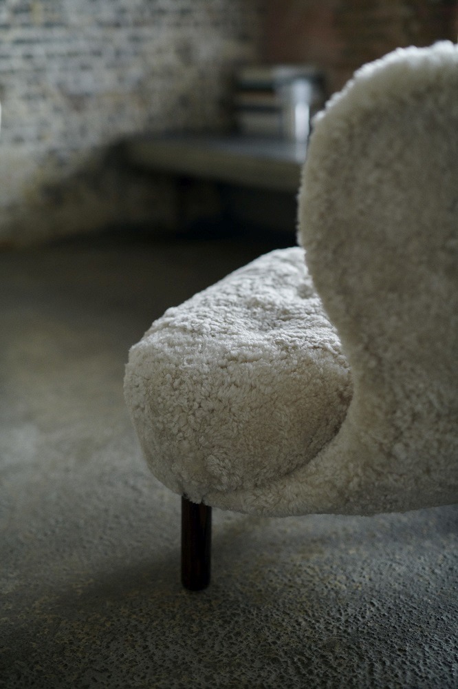 Detailaufnahme des Little Petra Sessels von AndTradition mit weichem, cremefarbenem Schaffellbezug und dunklen Holzbeinen.