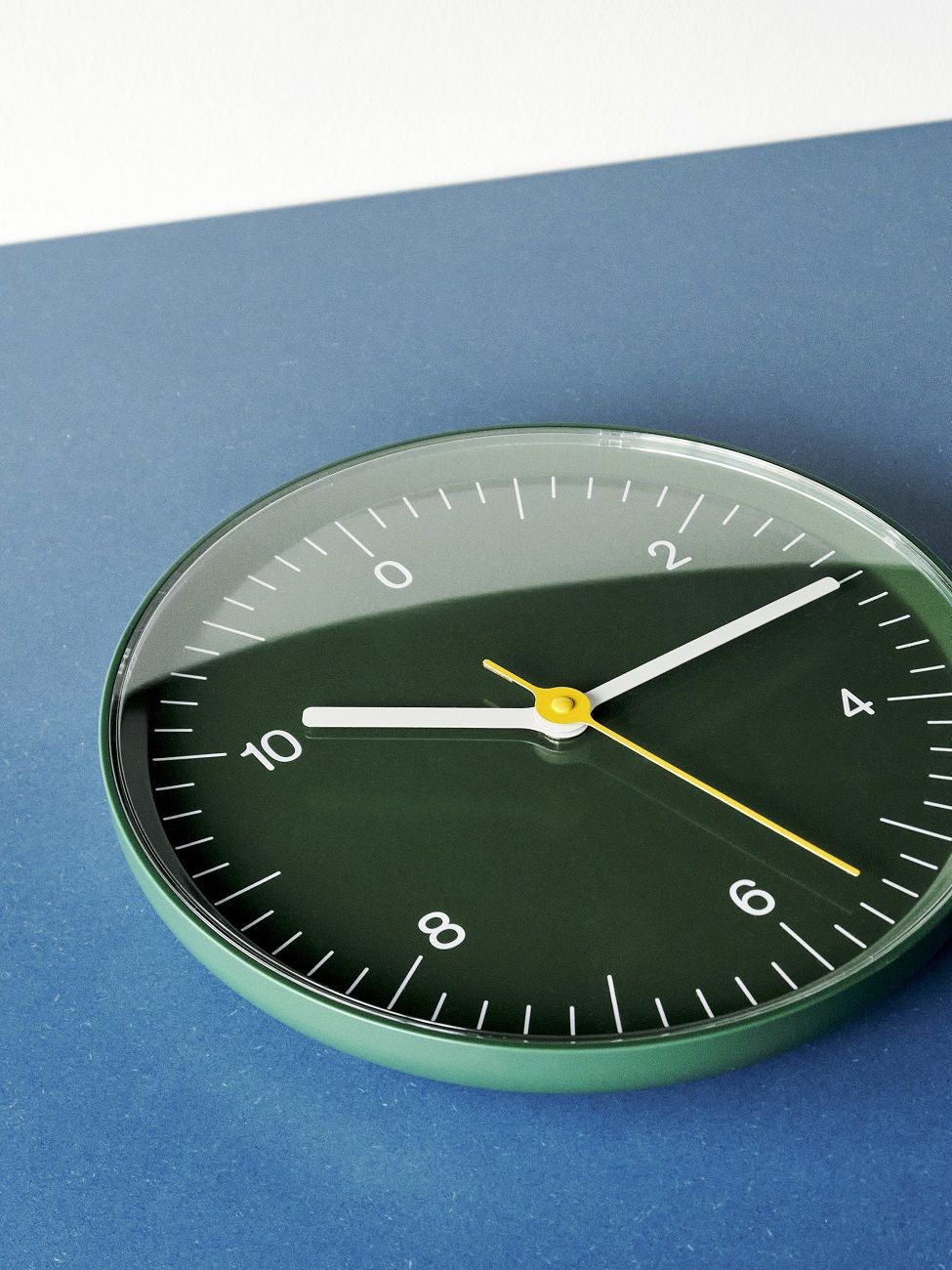 Grüne Hay Wanduhr mit minimalistischem Design und gelben Akzenten auf blauem Hintergrund.