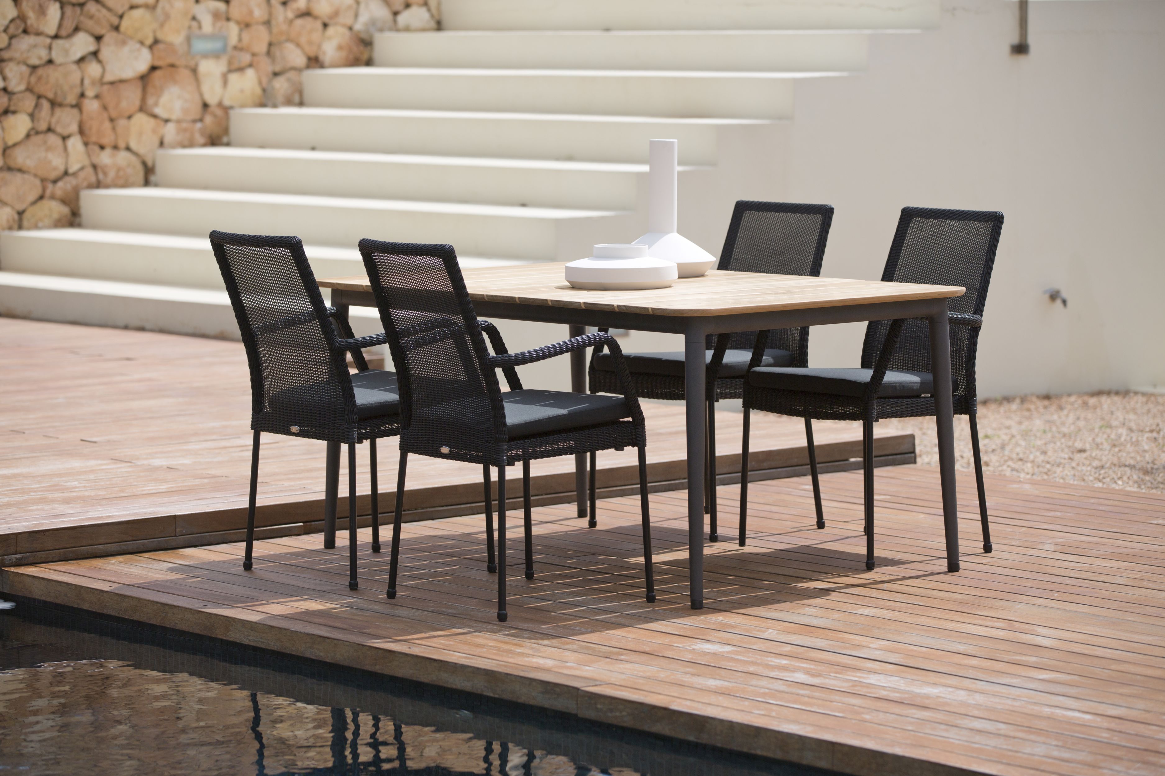 Core Outdoor Stuhl AirTouch von Cane-Line, taupefarben, mit Armlehnen, auf einer Terrasse mit Esstisch.
