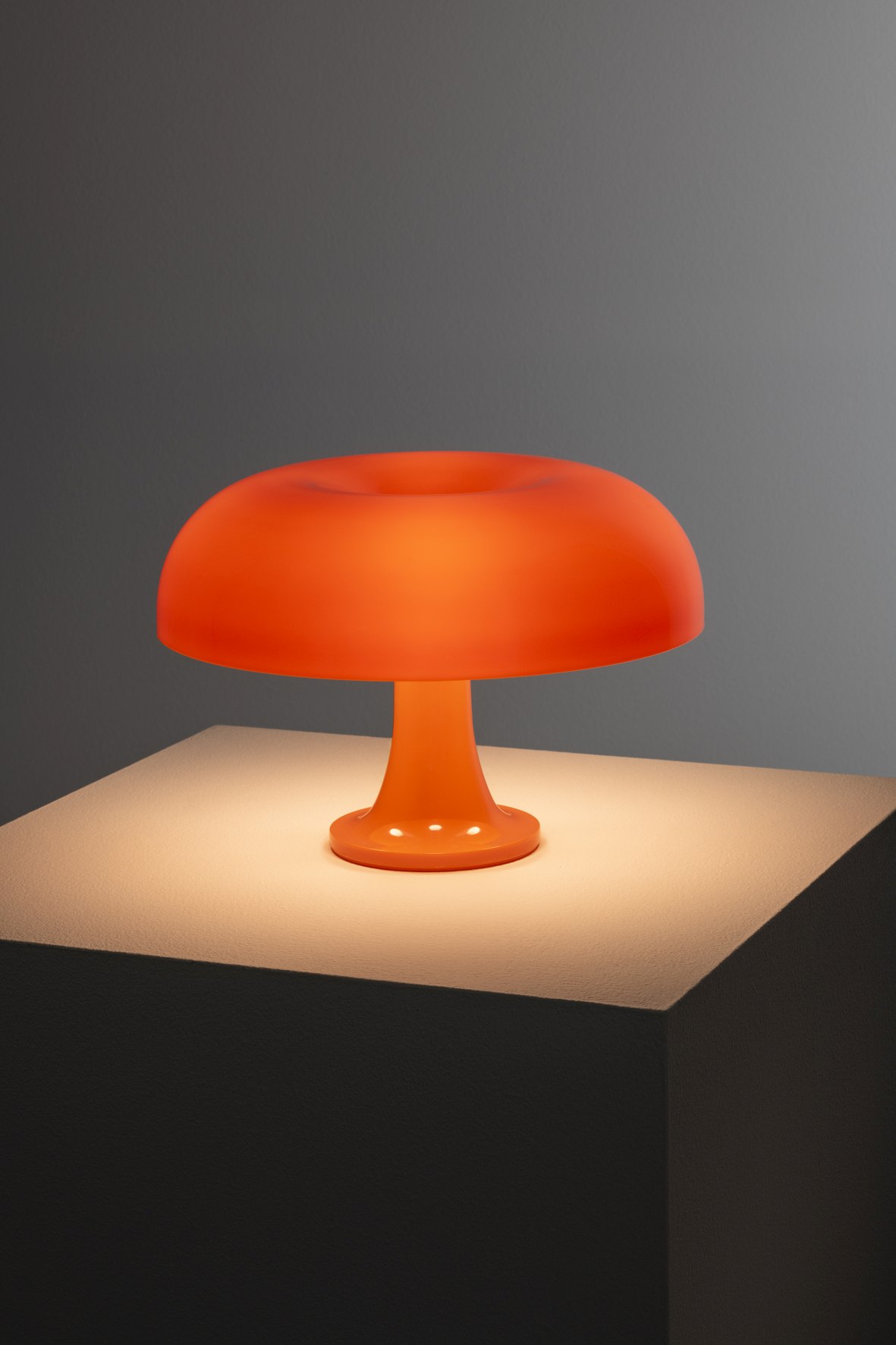 Orangefarbene Nessino Tischleuchte von Artemide auf einem Sockel, modernes Design, stimmungsvolle Beleuchtung.